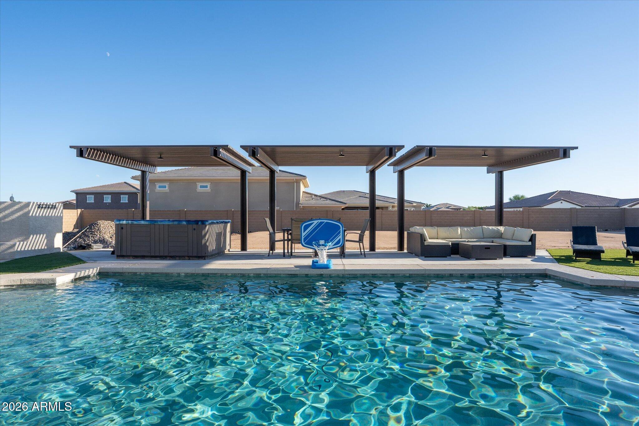 Backyard pool with a basketball hoop, hot tub, three shade structures, and patio seating.