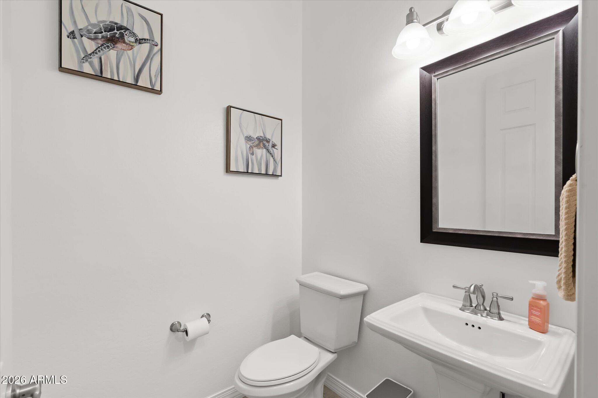 Bathroom with a white toilet and sink beneath a large dark-framed mirror.