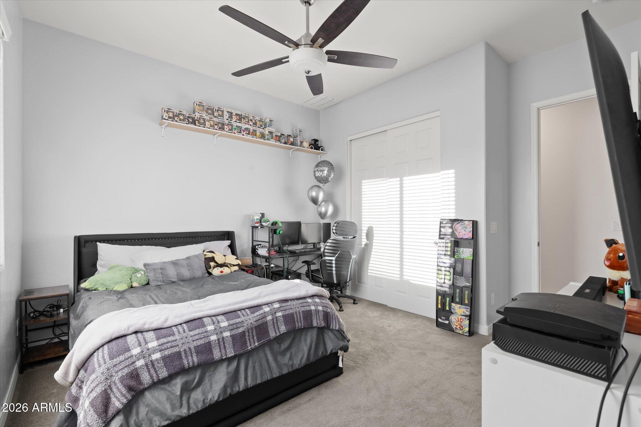 Bedroom with gray plaid bedding, a gaming desk, collectible figures, and sunlit closet doors.