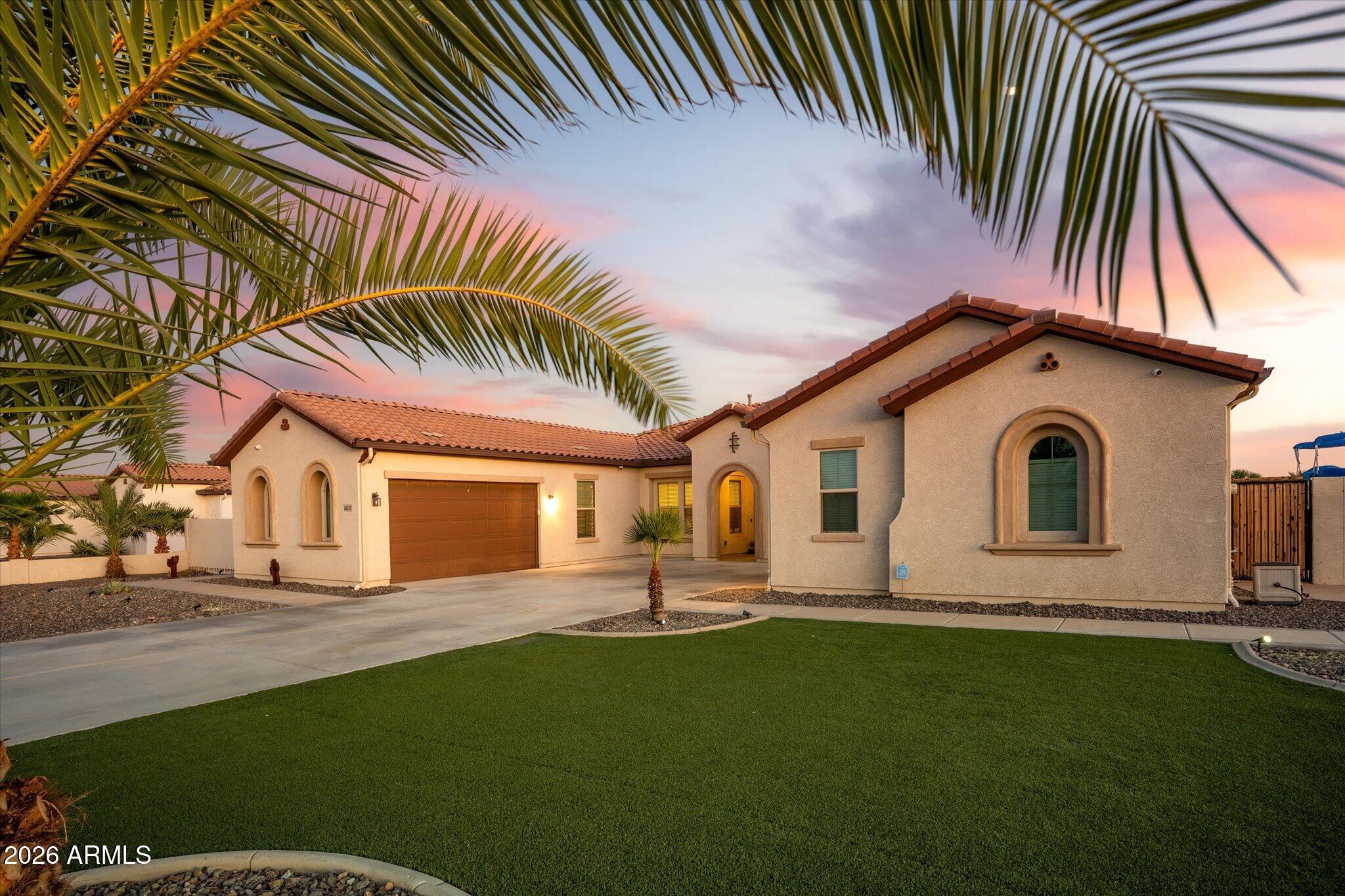 Stucco home with arched windows, tile roof, two-car garage, and palm-framed lawn at dusk.