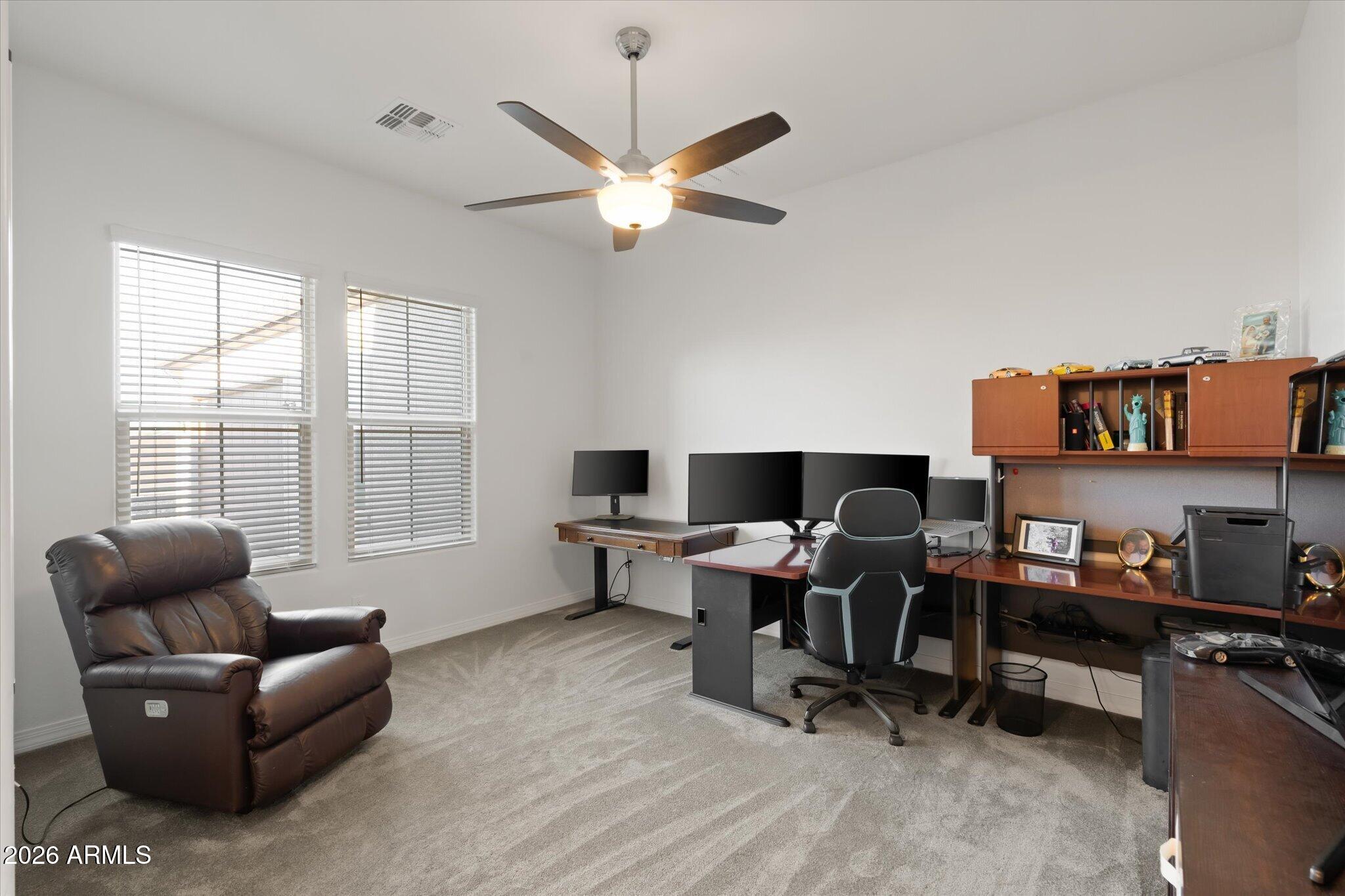 Home office with a leather recliner, multiple monitors, wood desks, and built-in shelving.