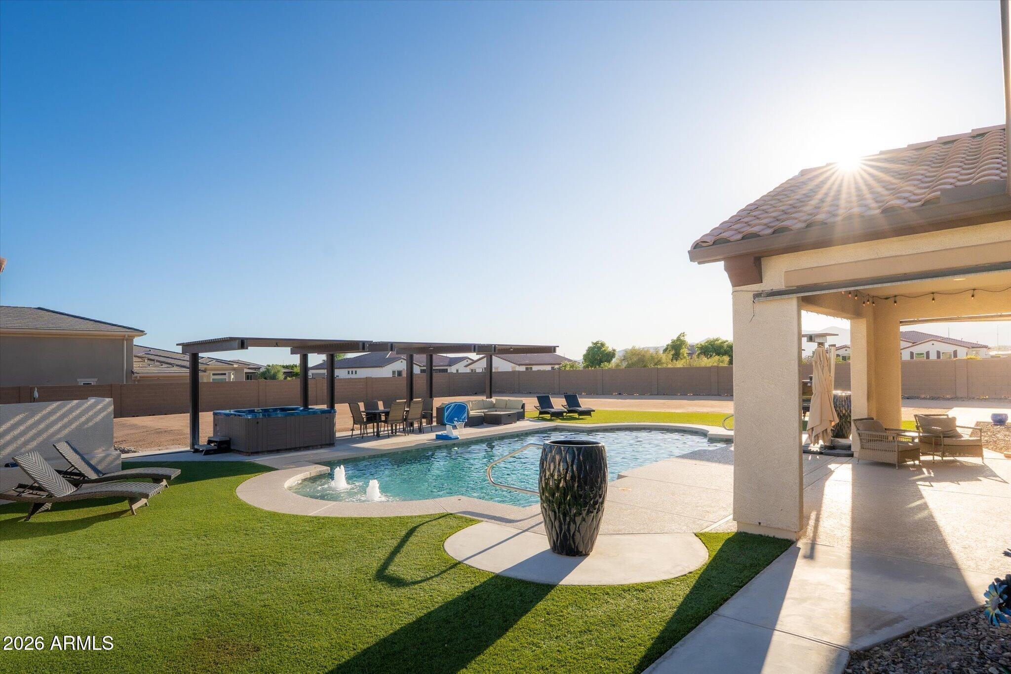 Backyard pool and spa with artificial turf, lounge chairs, and a covered patio in warm sunlight.