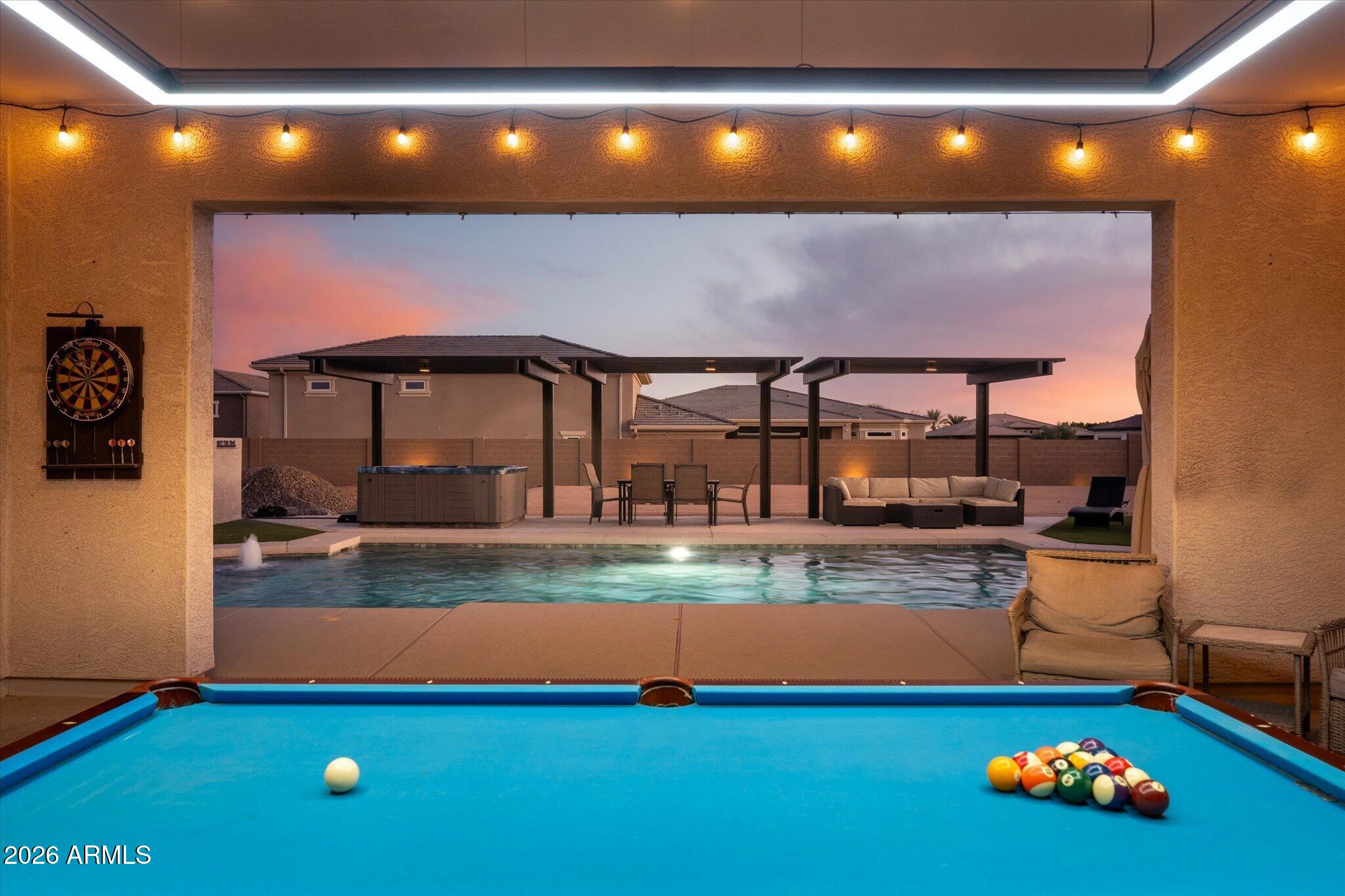 Backyard pool and billiards table beneath a covered patio at dusk.