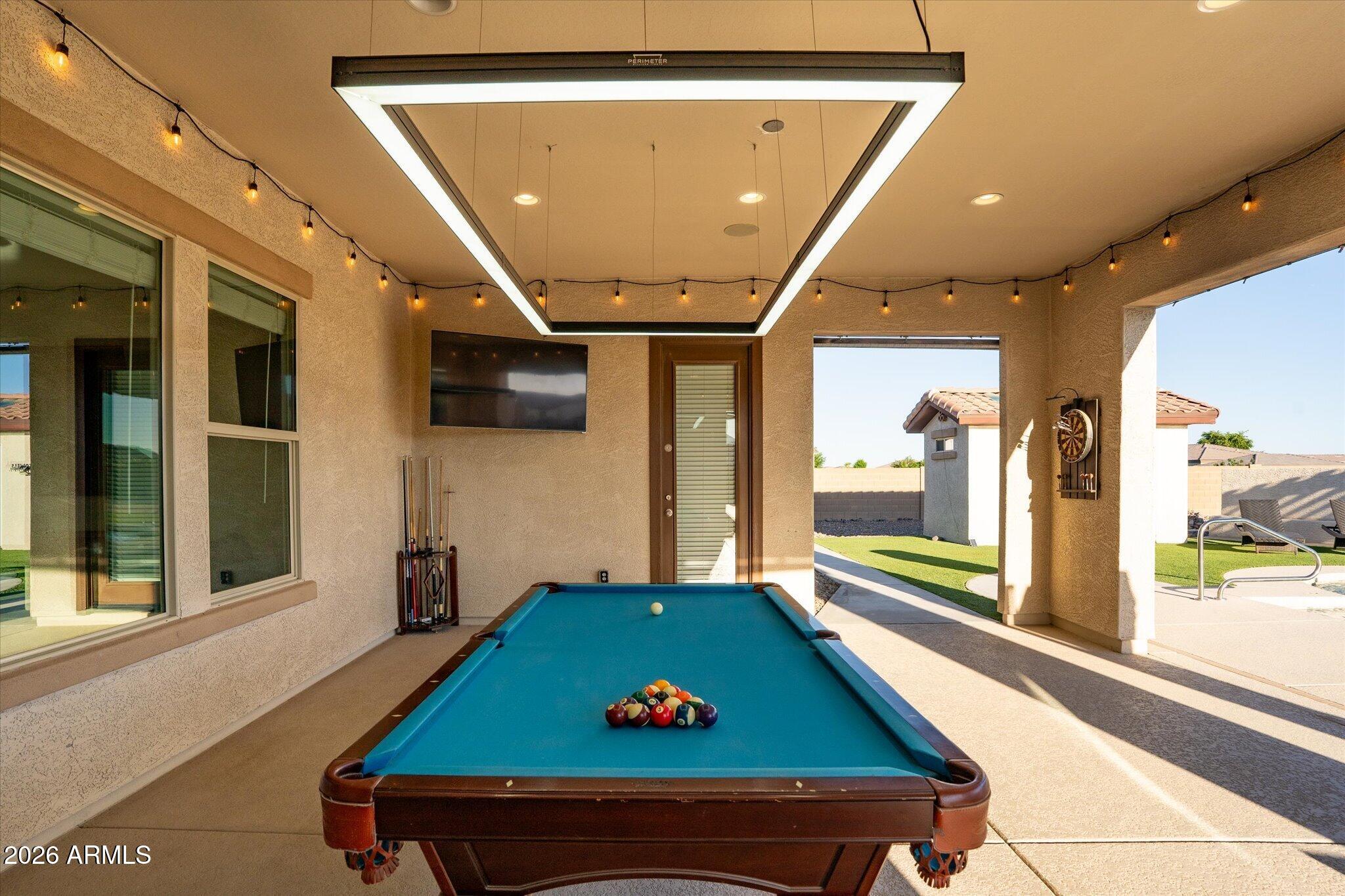Covered patio with a blue-felt pool table, string lights, and a view of the backyard pool.