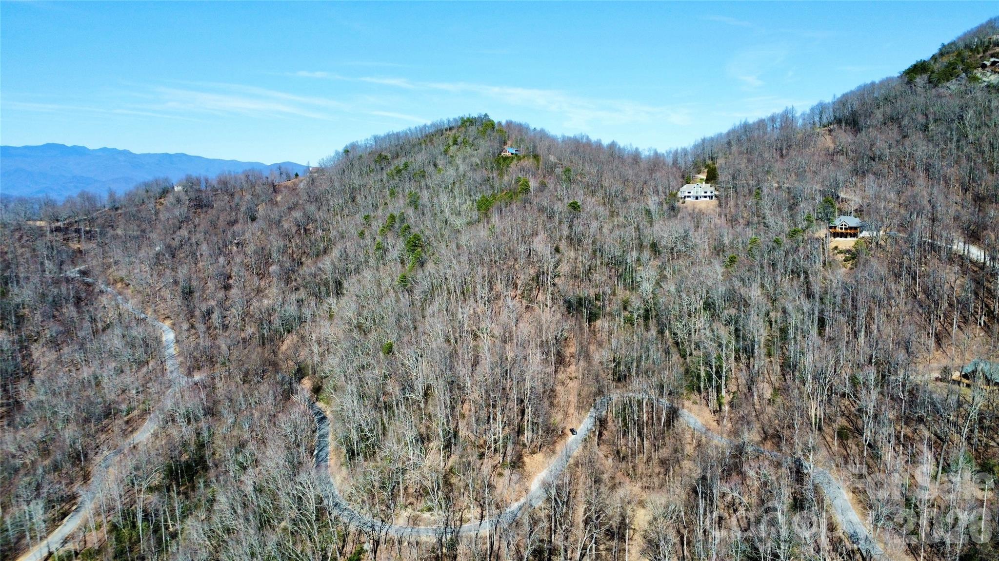 Aerial view of homes on a wooded mountain hillside, with winding roads and distant ridges.