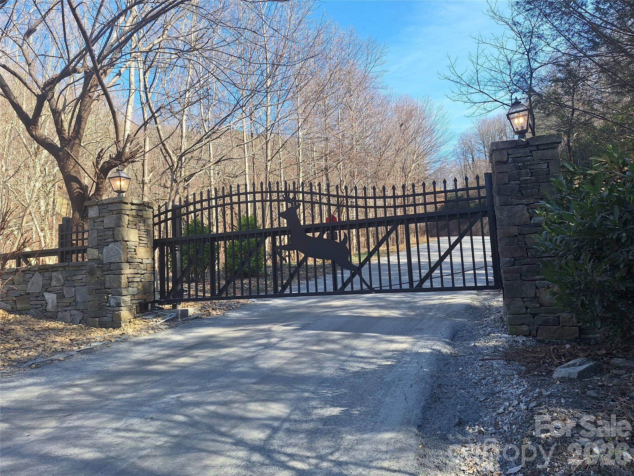 Residential driveway with a deer-silhouette iron gate between stone pillars and lanterns.
