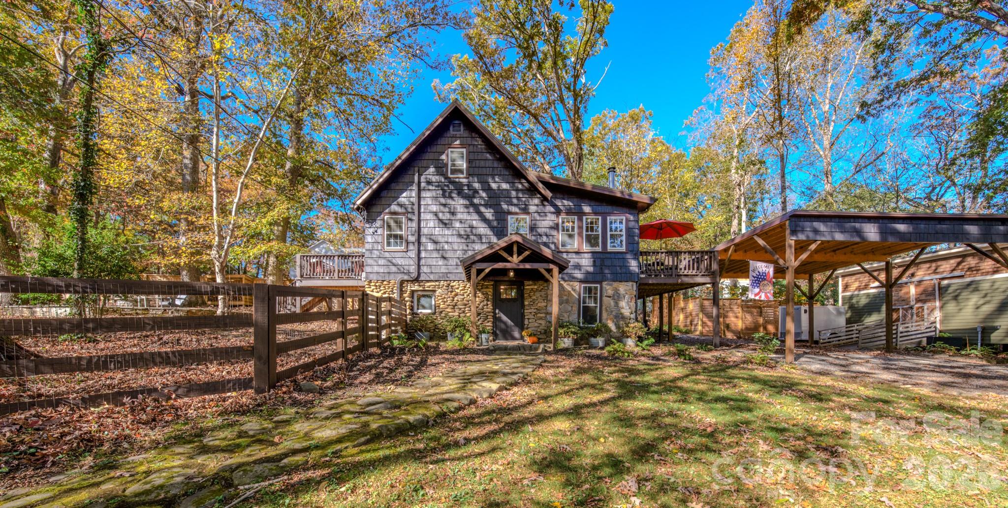 Dark-shingled home with a stone facade, elevated decks, and a covered carport amid autumn trees.
