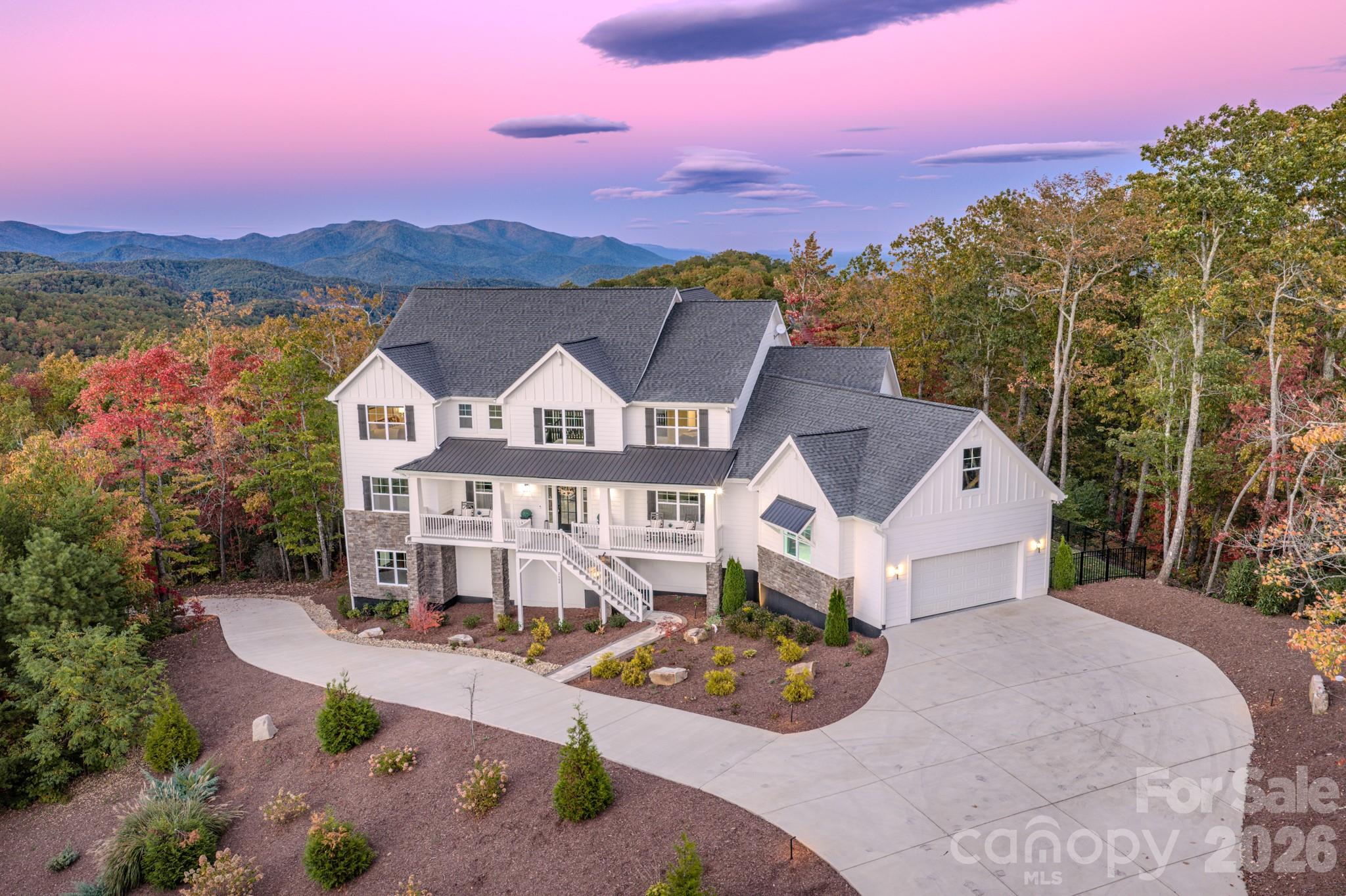 White multi-story home with stone accents, a broad driveway, and autumn trees against a mountain backdrop.