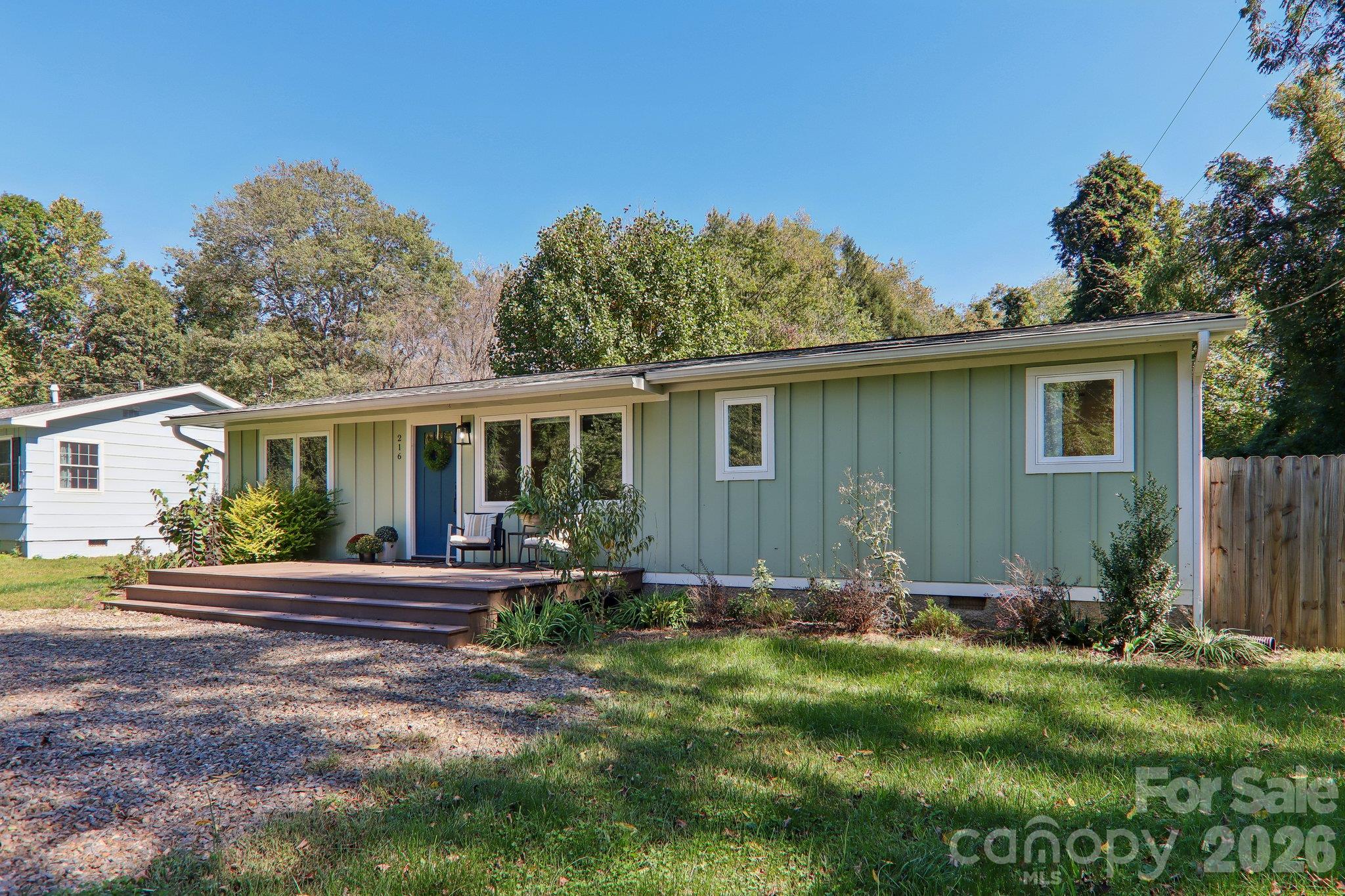 Single-story green home with a blue front door, raised wooden porch, and landscaped yard.
