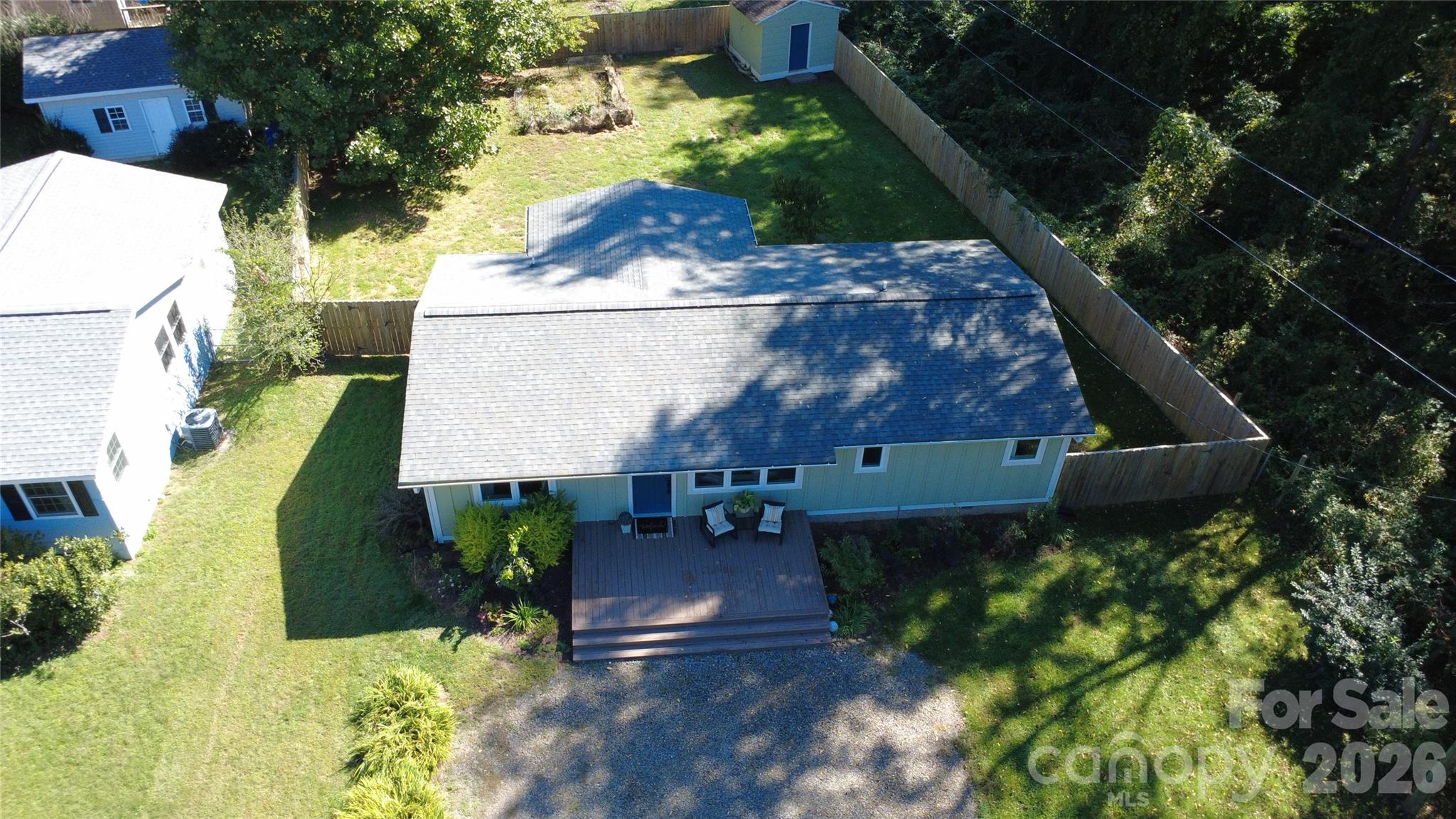 Aerial view of a single-story home with a fenced yard, raised deck, and gravel driveway.