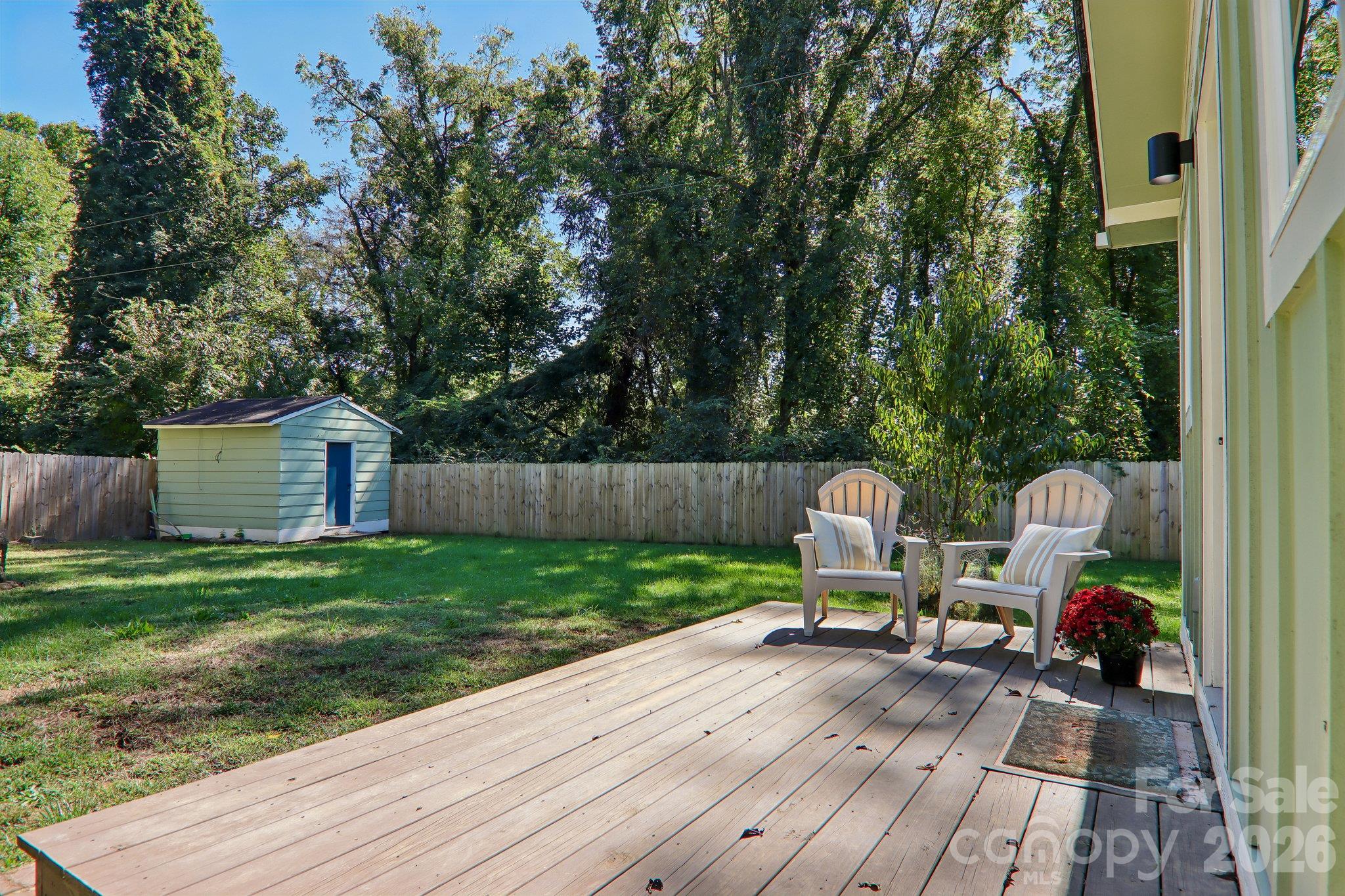 Backyard deck with two chairs overlooking a fenced lawn and storage shed.