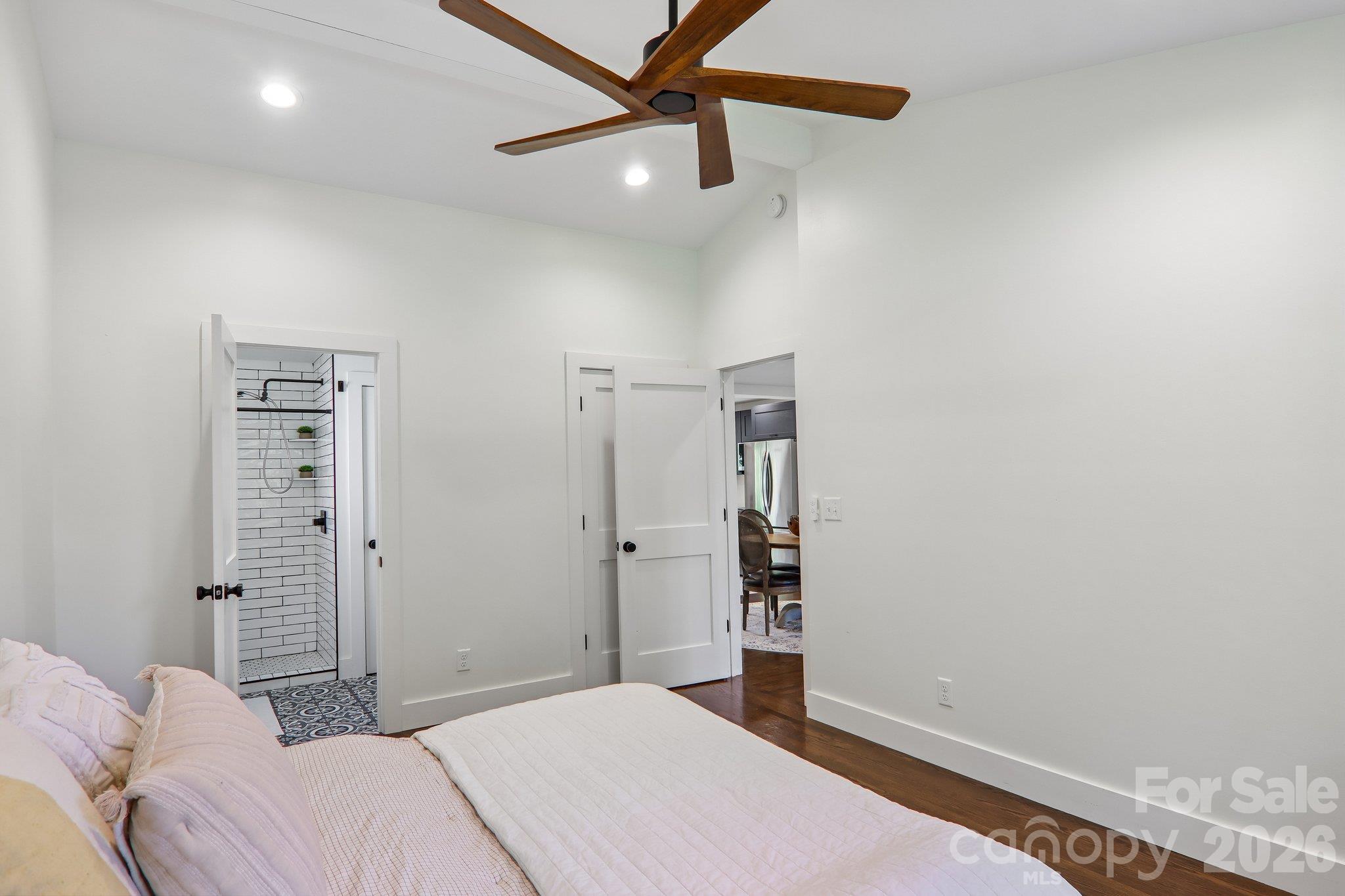 Bedroom with a wood-blade ceiling fan and open doorway to a subway-tile shower.