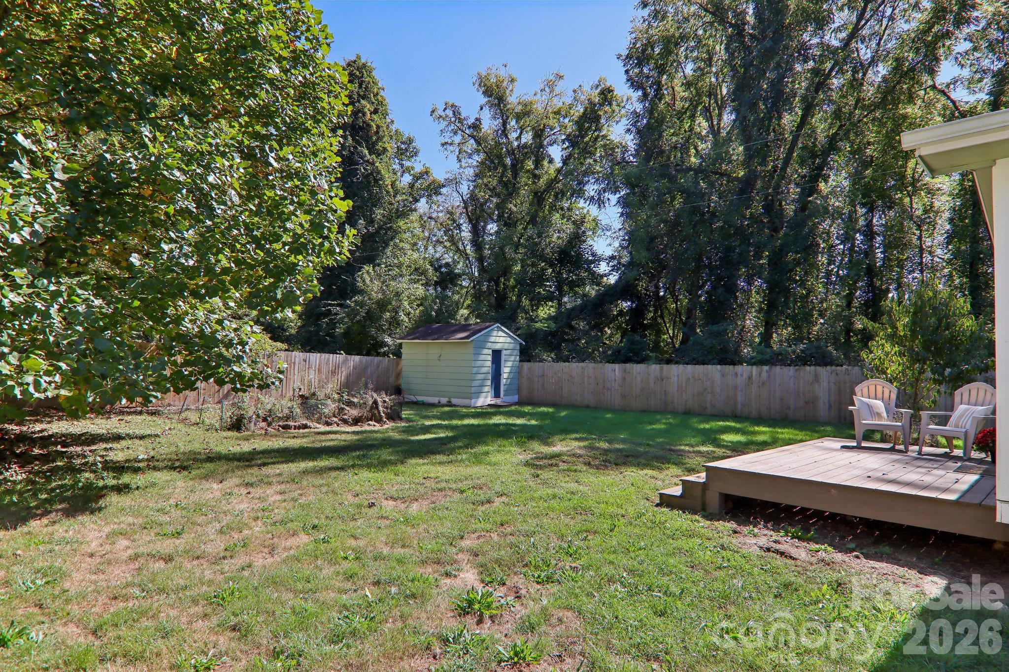 Backyard with a fenced lawn, storage shed, and raised deck with chairs.