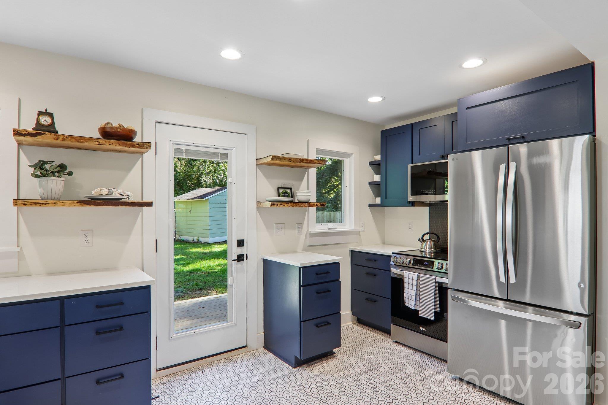 Kitchen with navy cabinets, open wood shelves, stainless steel appliances, and a glass door to the yard.