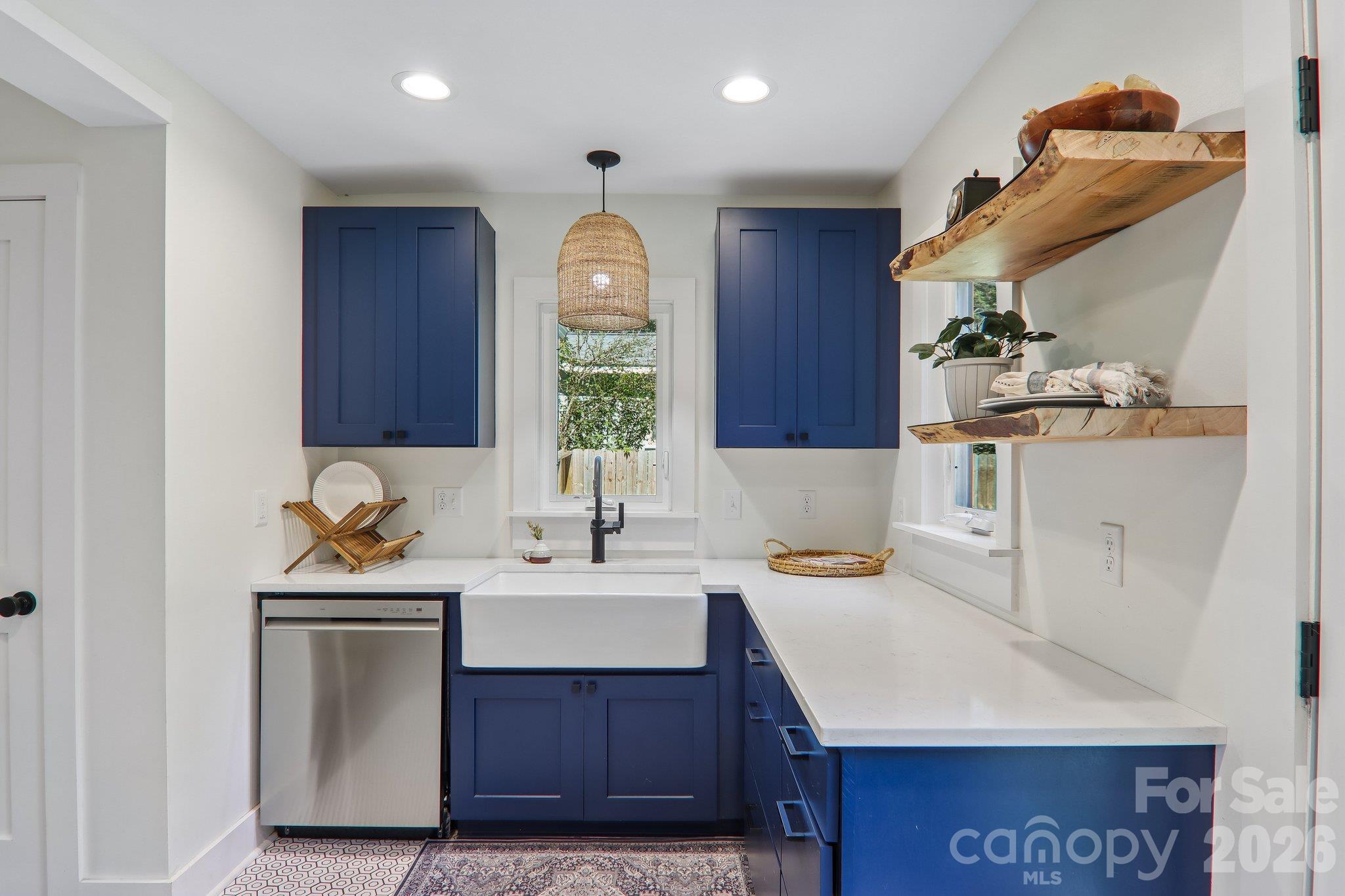 Kitchen with navy cabinets, farmhouse sink, white counters, and rustic wood shelves.