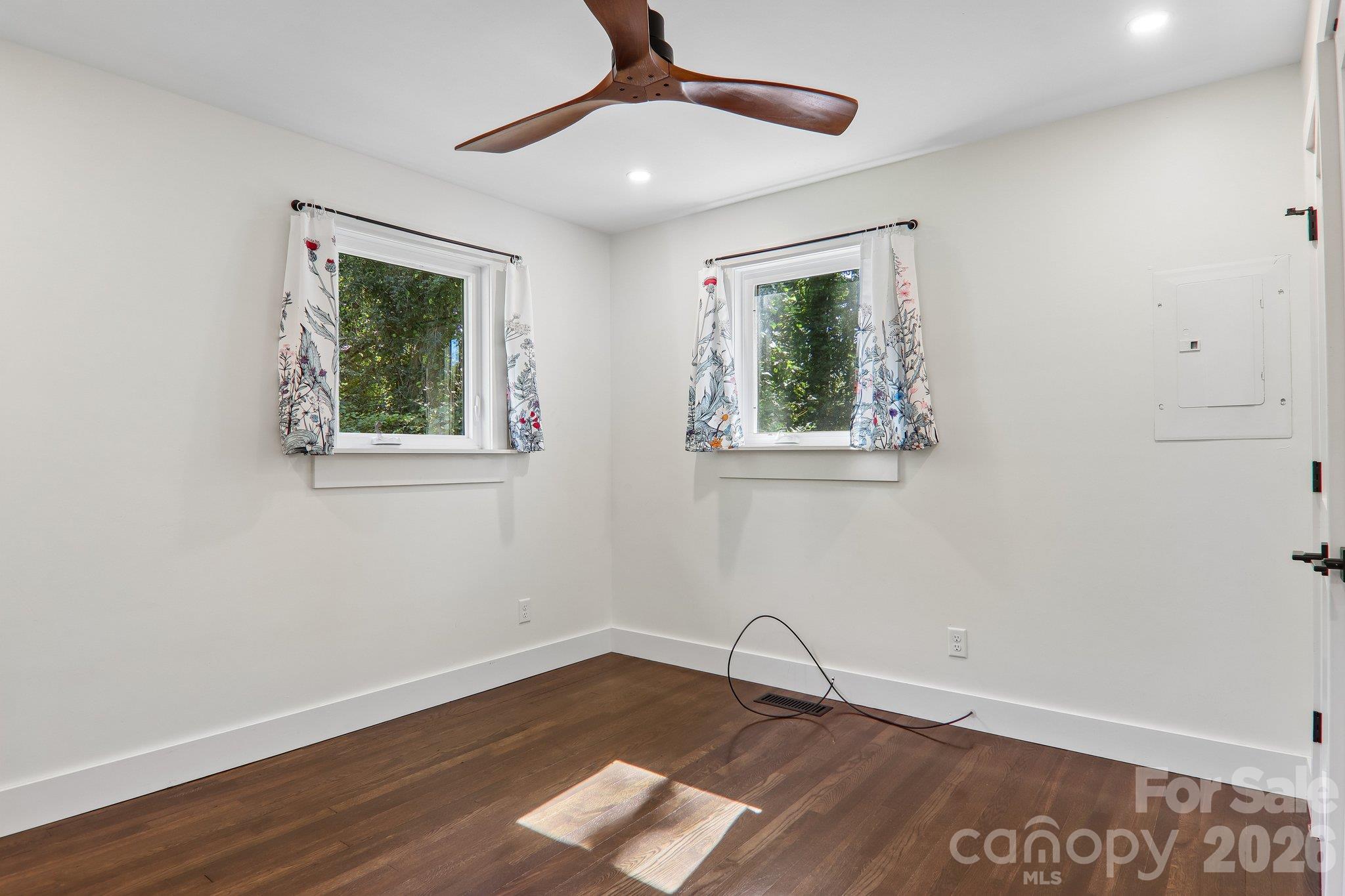 Vacant room with dark wood floors, two curtained windows, and a wood ceiling fan.