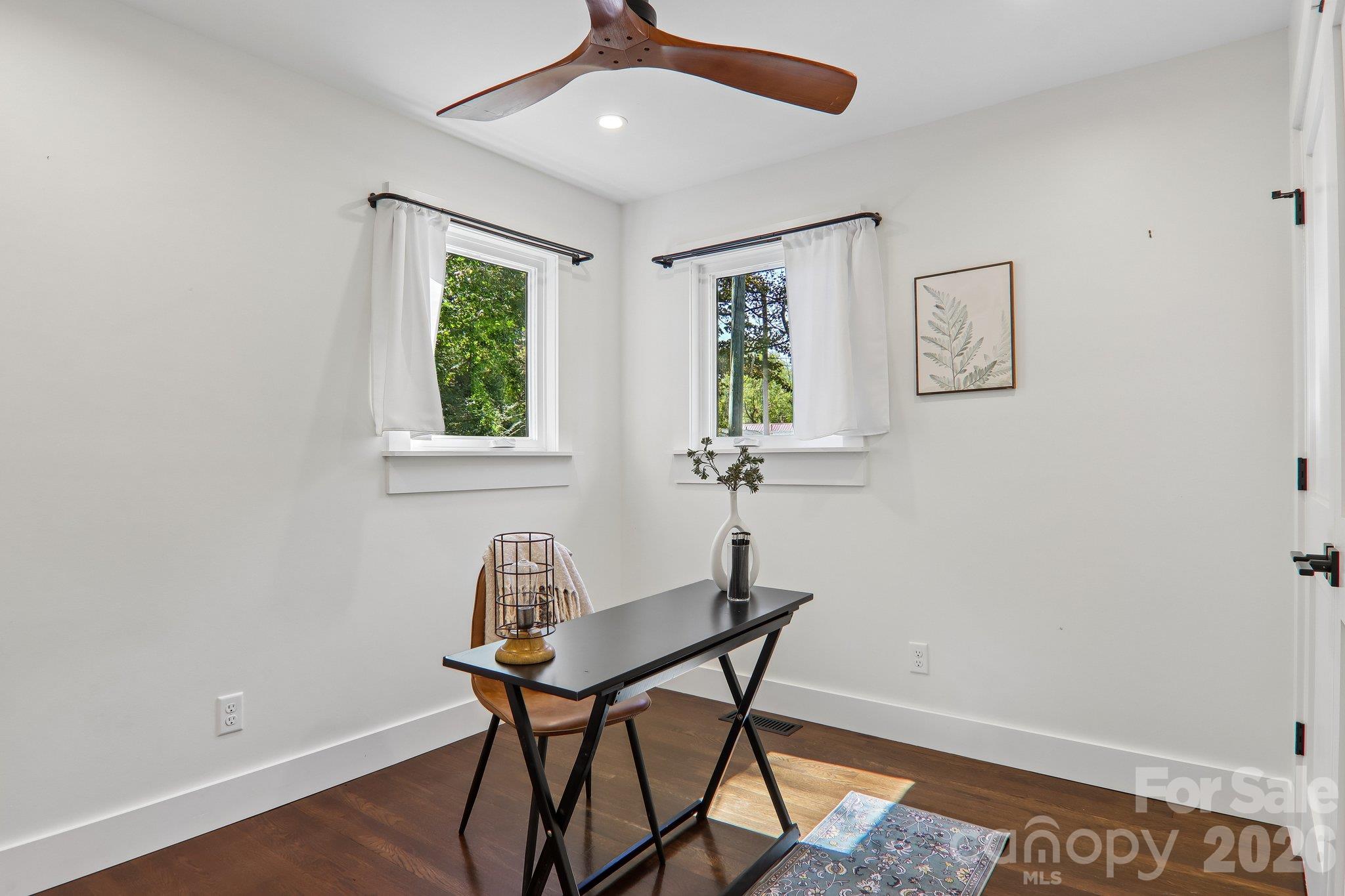 Staged home office with a black desk between two curtained windows and a wooden ceiling fan.