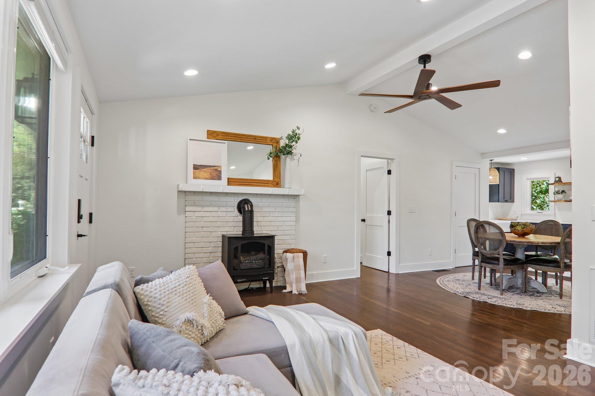 Living room with a white brick fireplace and black stove, opening into a dining area.