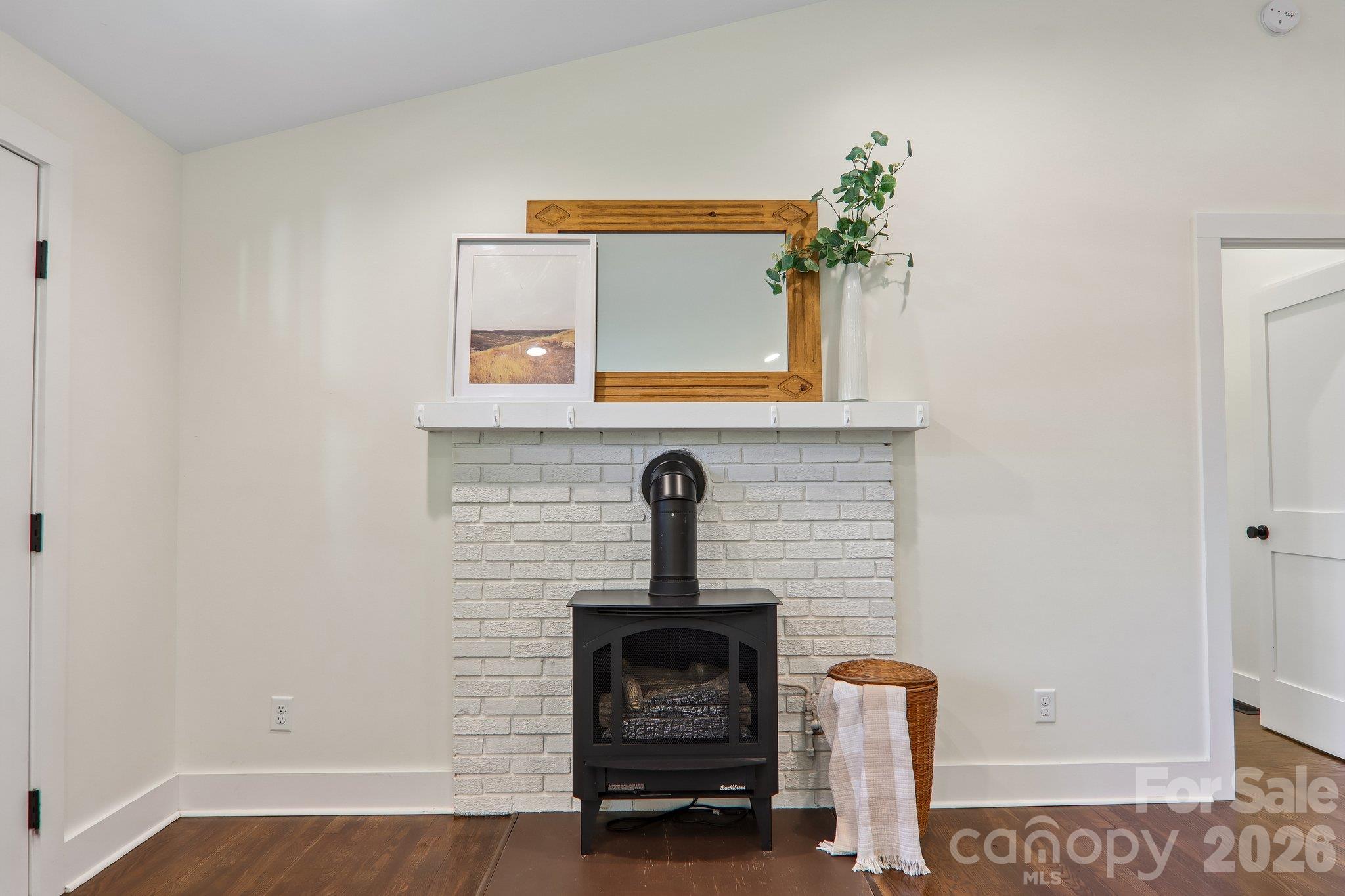 Black freestanding stove against a white brick fireplace, with a wood-framed mirror and basket beside it.
