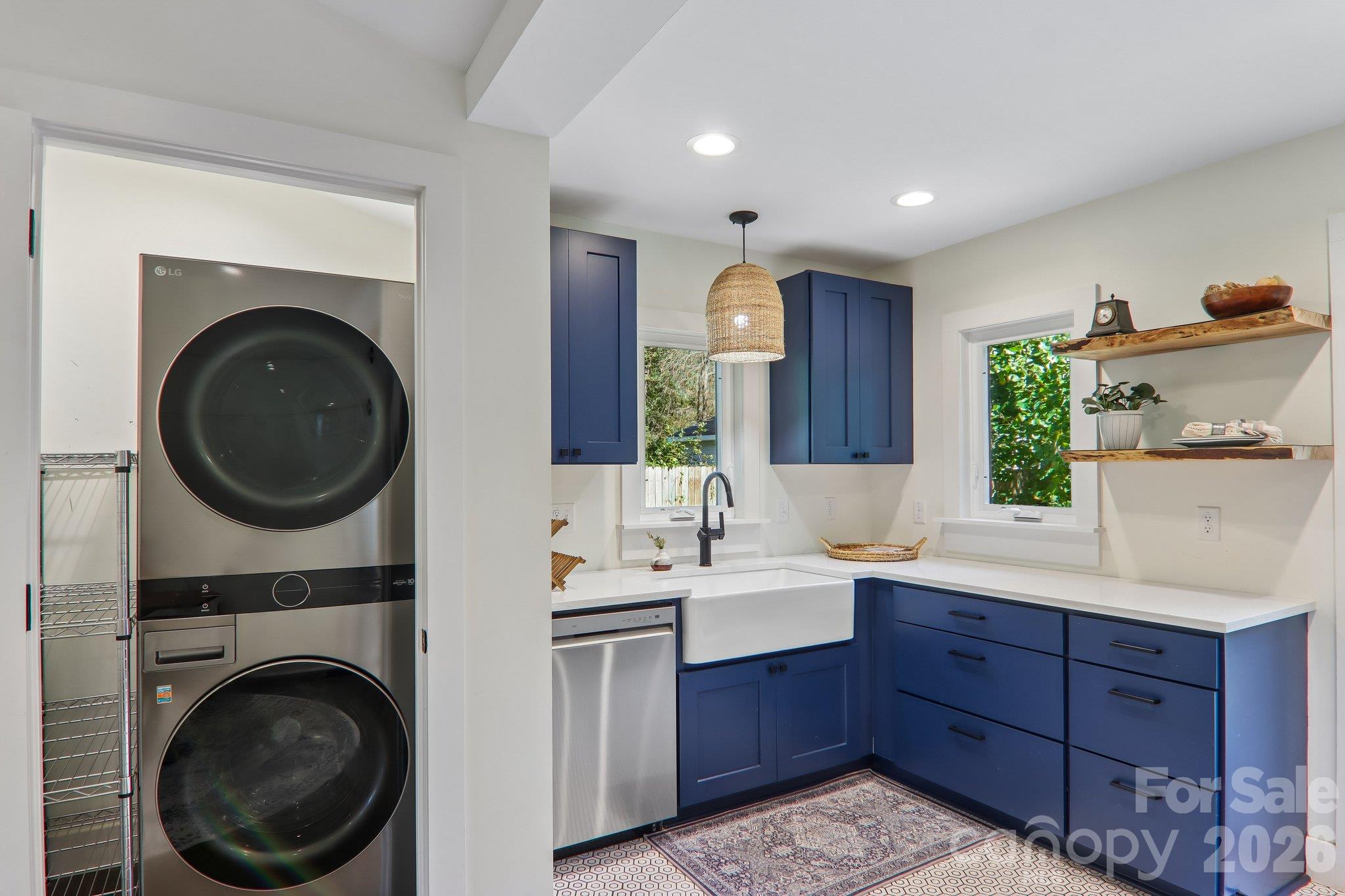 Kitchen with deep blue cabinets, farmhouse sink, and stacked washer and dryer.