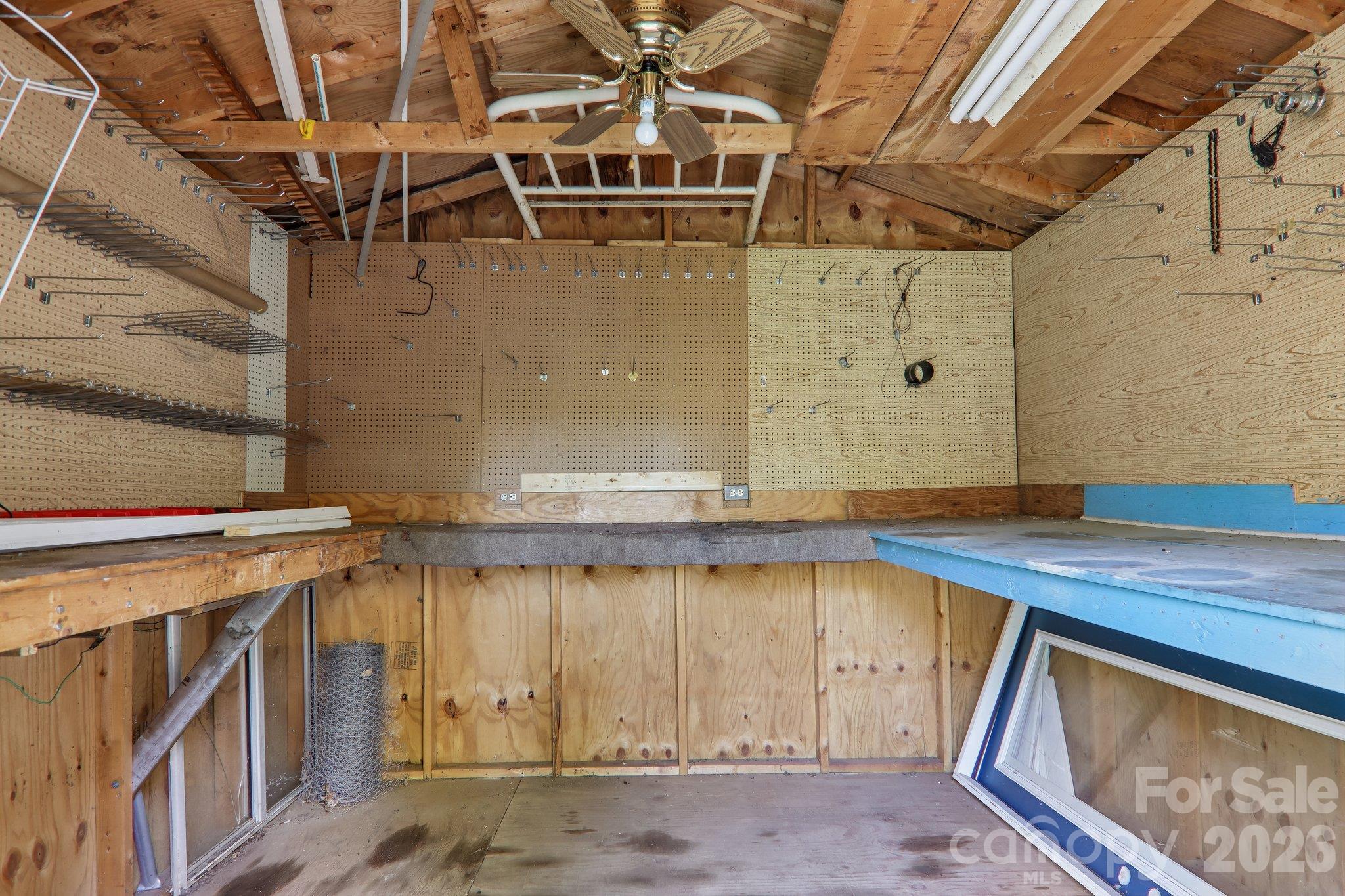 Garage workshop with exposed rafters, pegboard walls, storage hooks, and a blue workbench.