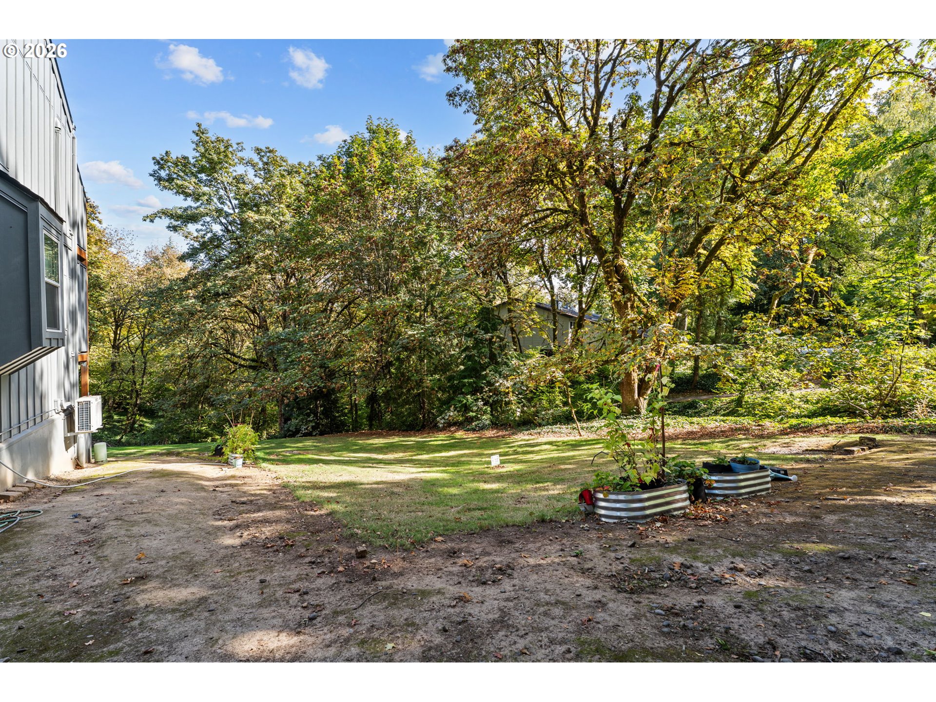 Residential yard with mature trees, a small lawn, and corrugated metal raised garden beds.