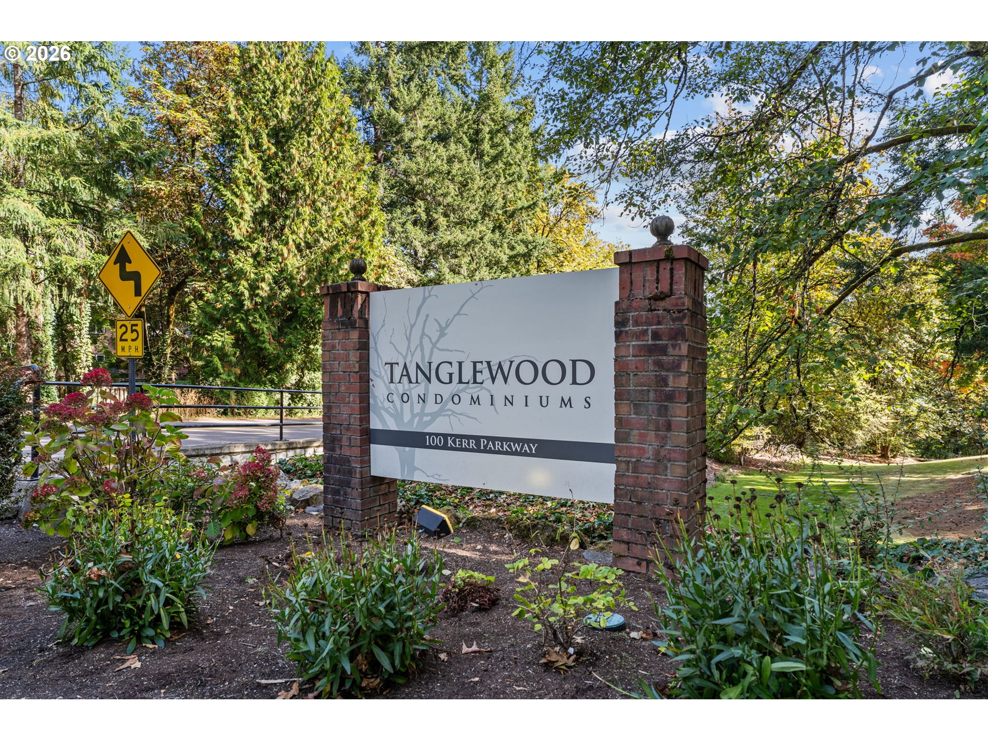 Tanglewood Condominiums entrance sign between brick pillars, surrounded by mature trees and landscaped grounds.