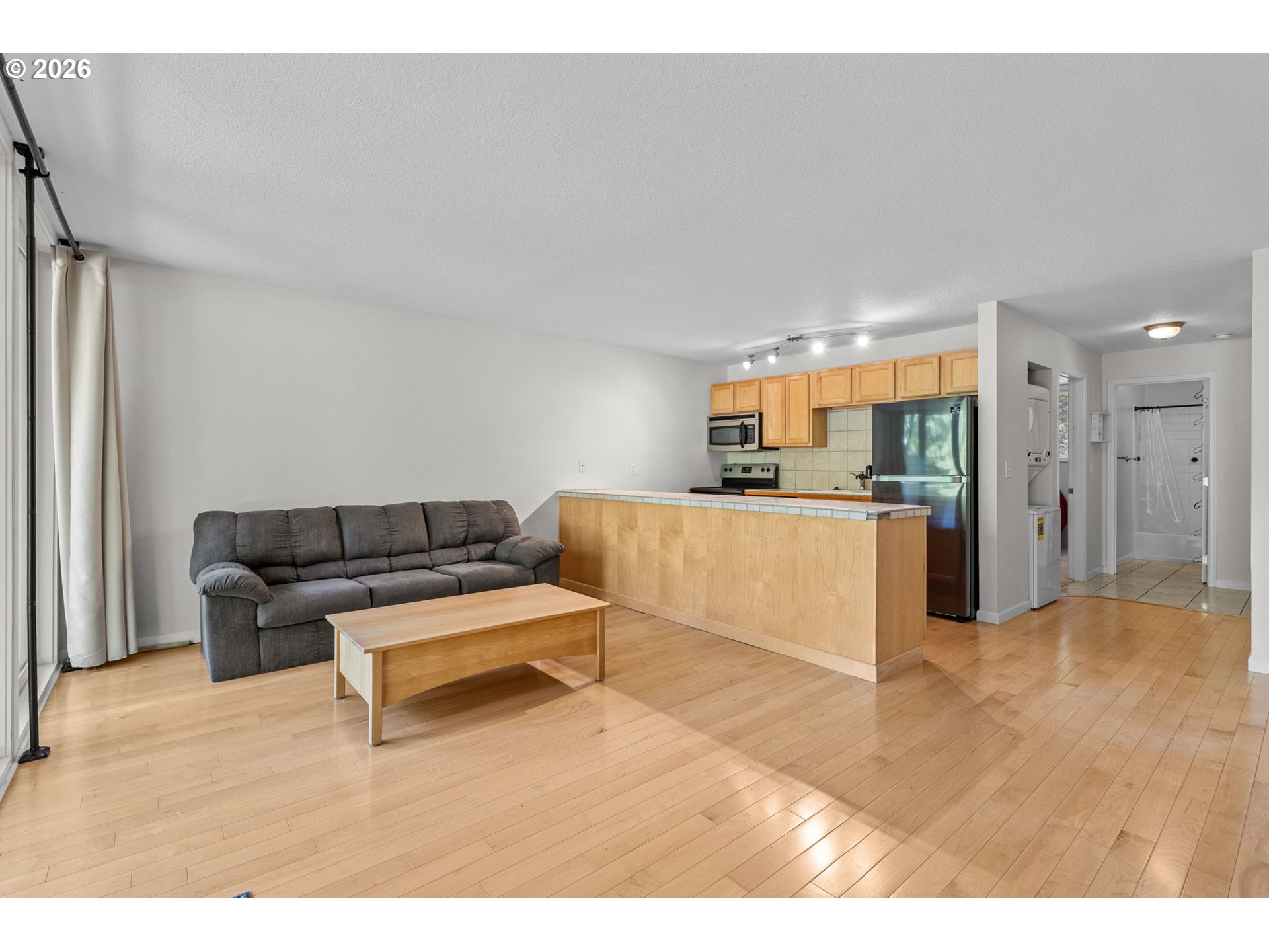Open-plan living room and kitchen with a gray sofa, wood breakfast bar, and light hardwood floors.