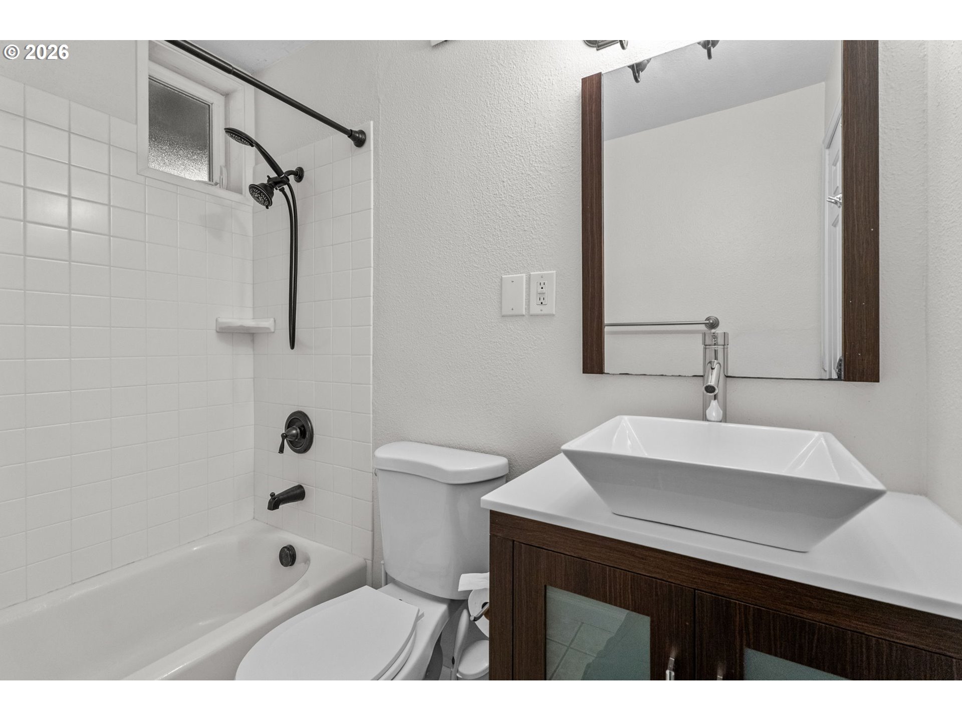 Bathroom with a tiled tub and shower, frosted window, and vessel sink on a dark wood vanity.