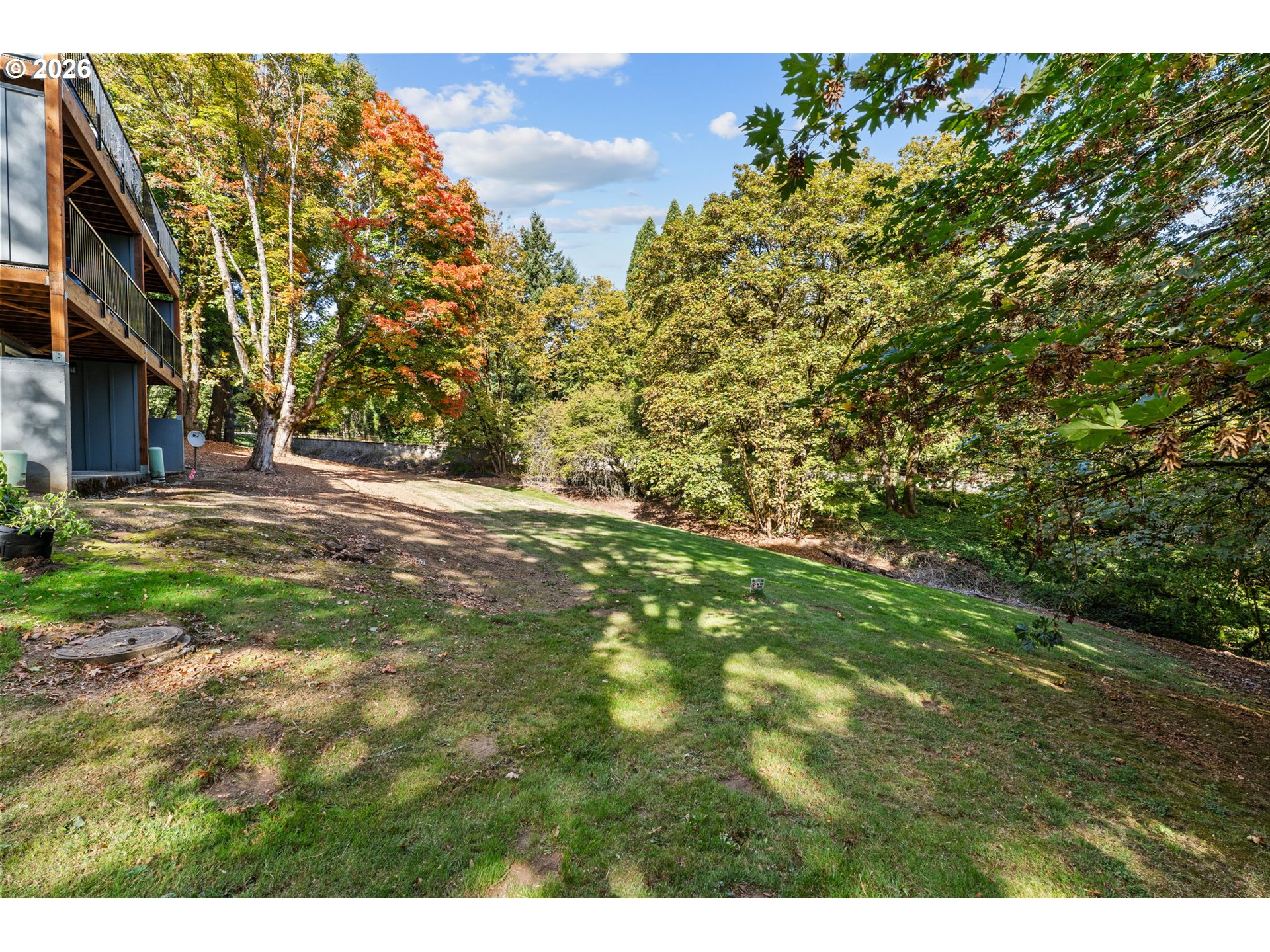 Sloped grassy yard with mature autumn trees and an elevated wooden deck beside the building.