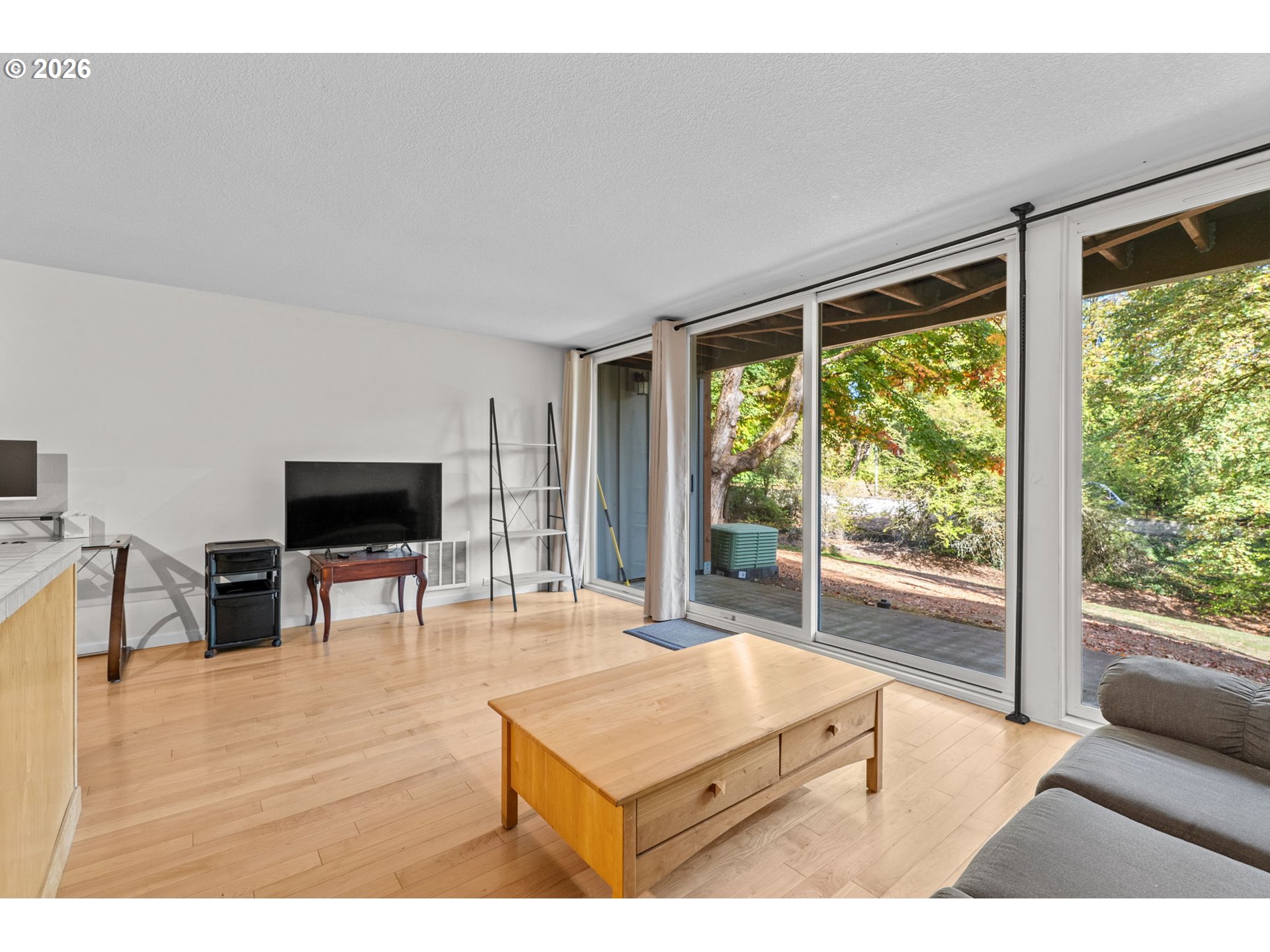 Living room with hardwood floors and wide sliding glass doors overlooking trees.