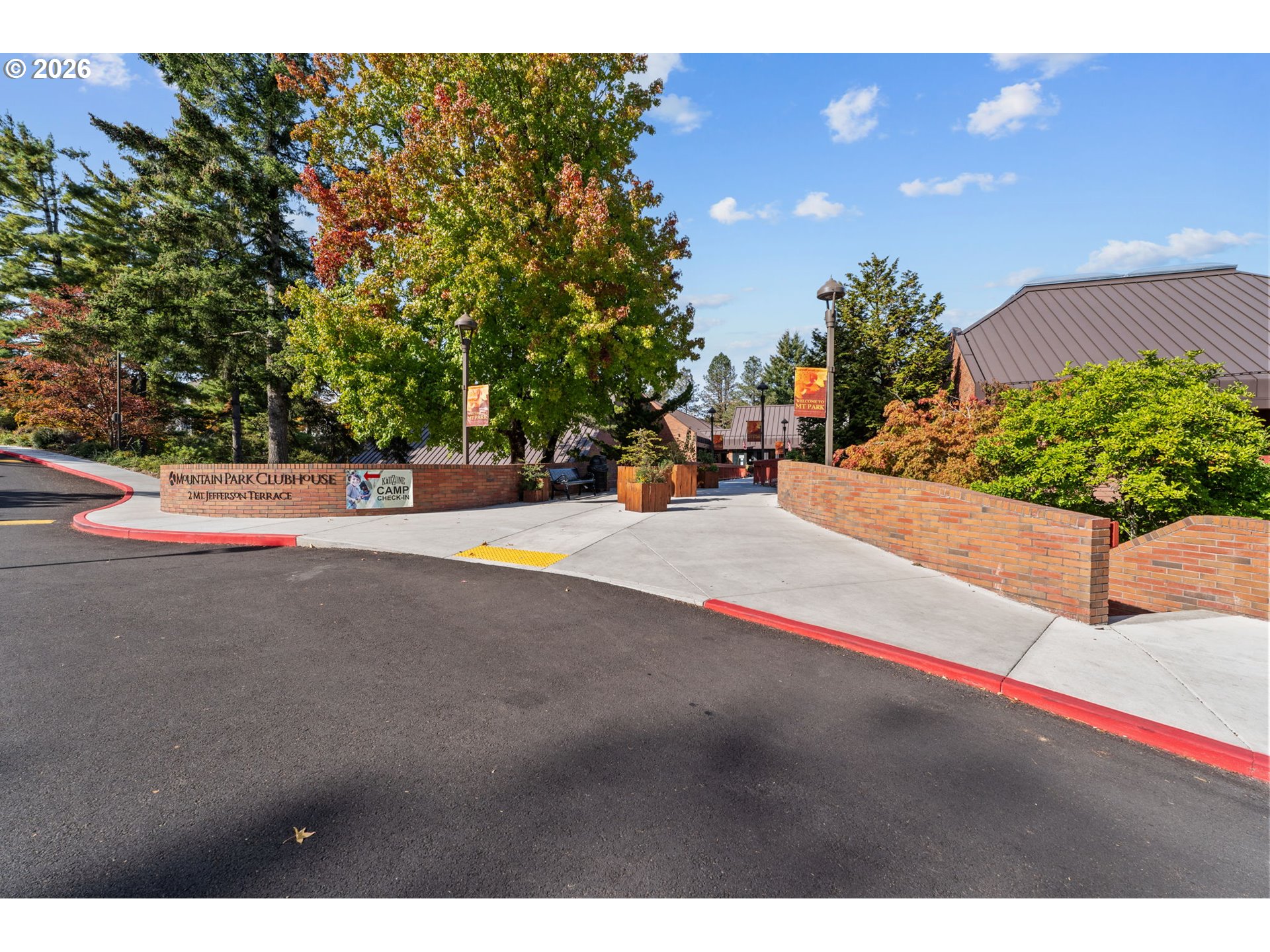 Mountain Park Clubhouse entrance with brick walls, a broad walkway, and colorful autumn trees.