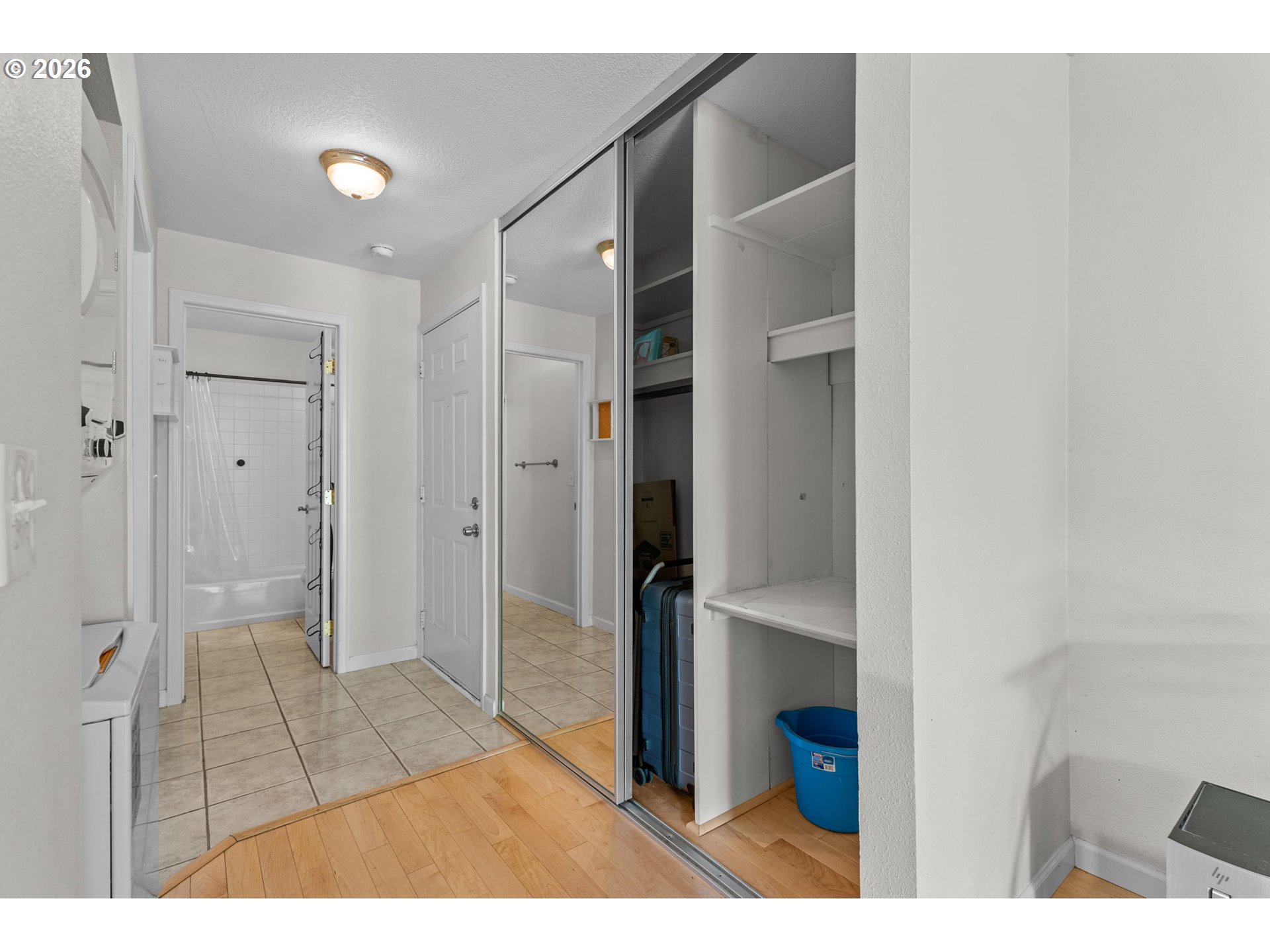 Closet and dressing area with mirrored sliding doors and built-in shelves beside a tiled bathroom.