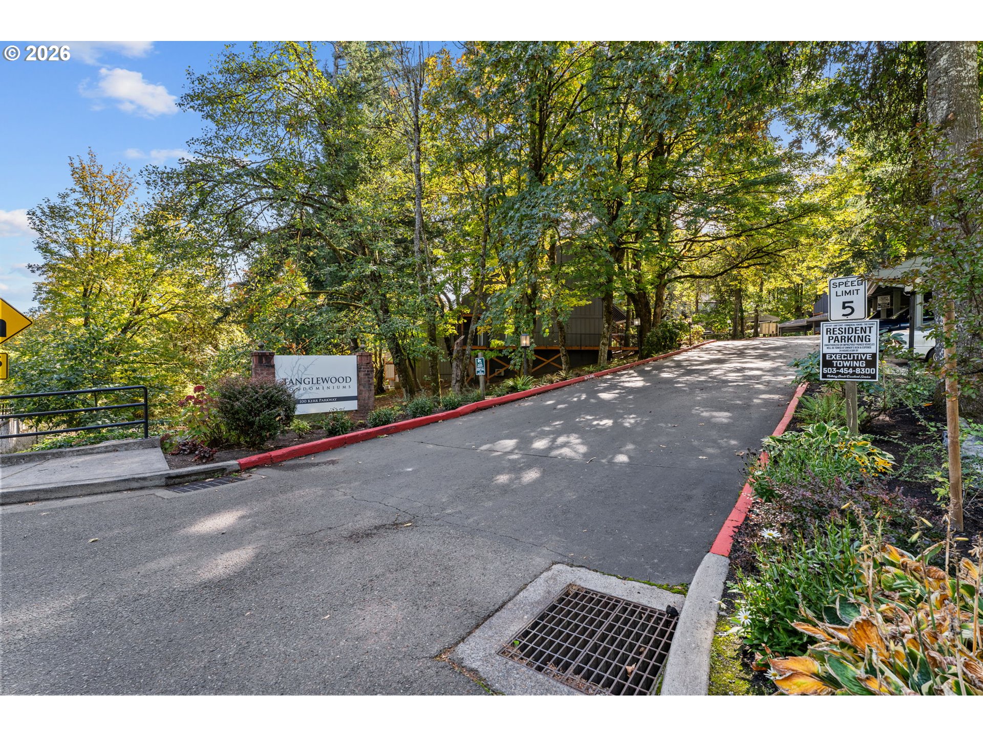 Tree-lined entrance to Tanglewood Condominiums with a monument sign and landscaped driveway.