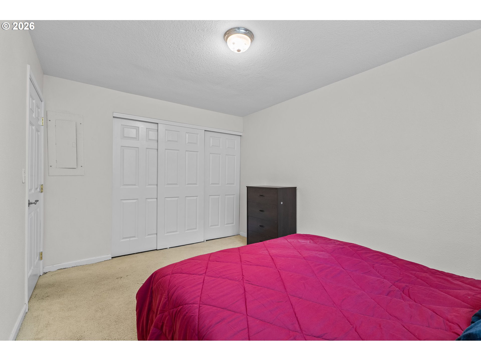 Bedroom with a bright pink quilt, white sliding closet doors, and a dark chest of drawers.