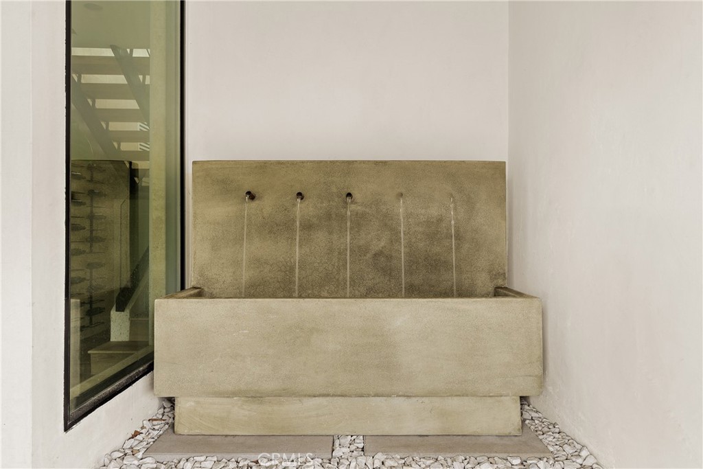 Concrete courtyard fountain with narrow water streams, pale pebble landscaping, and a large glass window.