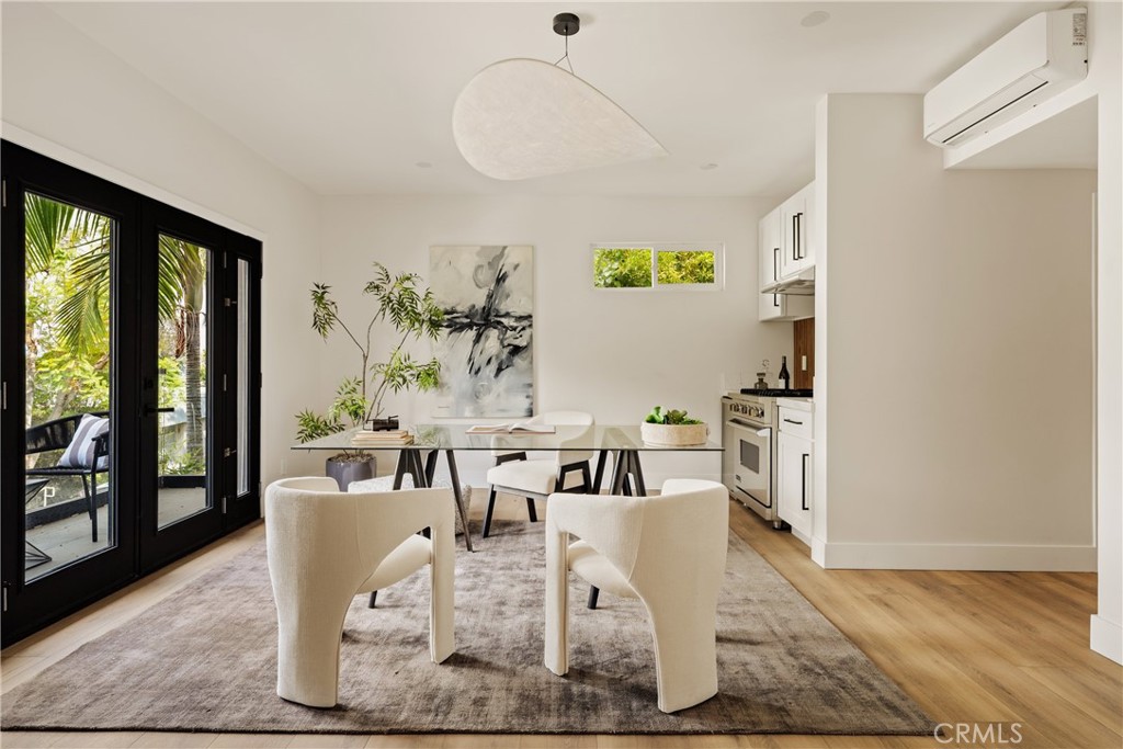 Dining area with a glass-top table, upholstered chairs, and black-framed doors opening to greenery.