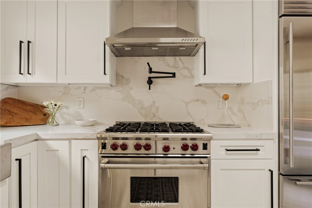 Kitchen with a stainless-steel gas range, white cabinets, and veined marble backsplash.