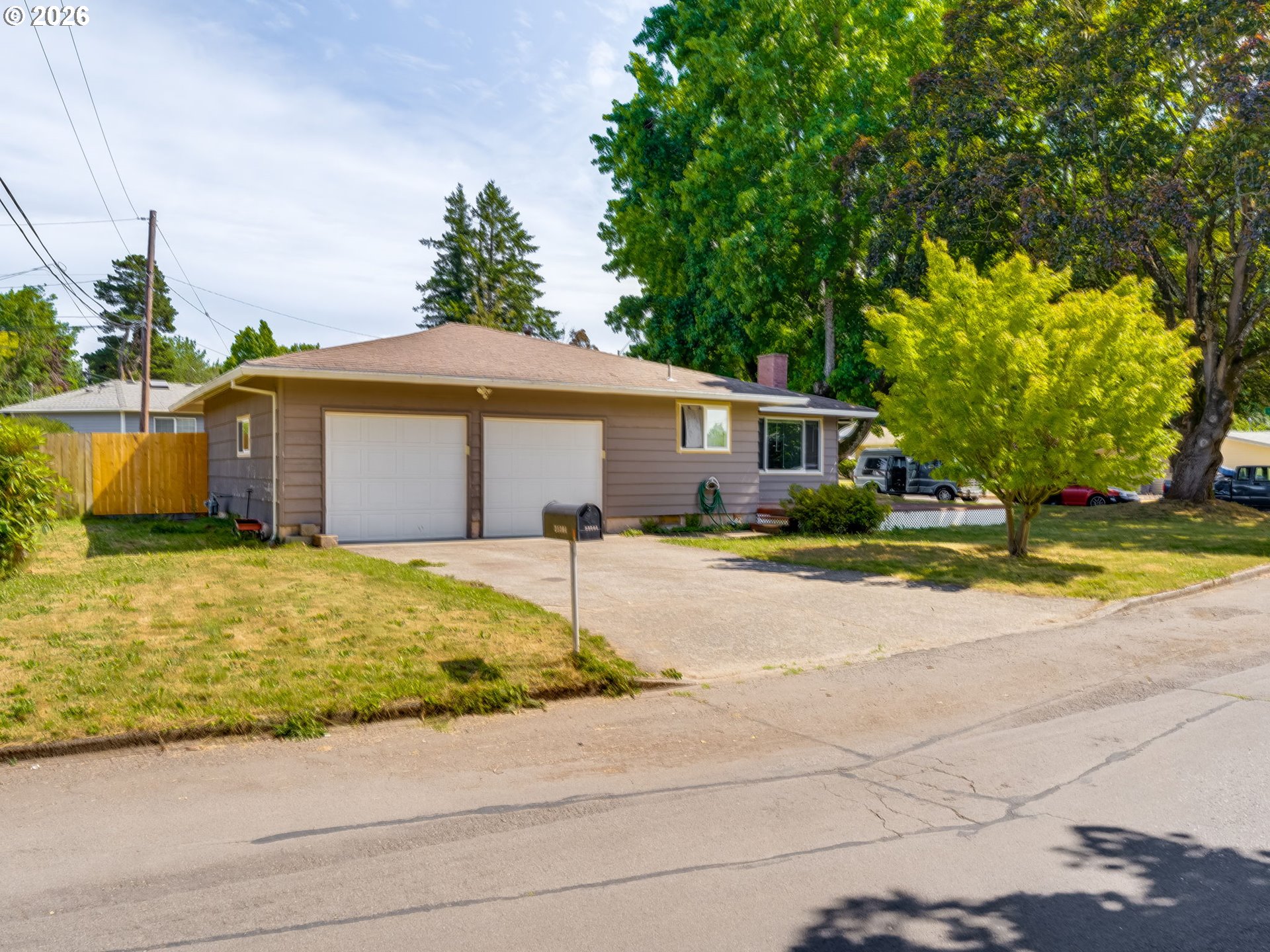 Single-story taupe house with a double garage, wide driveway, and mature trees.
