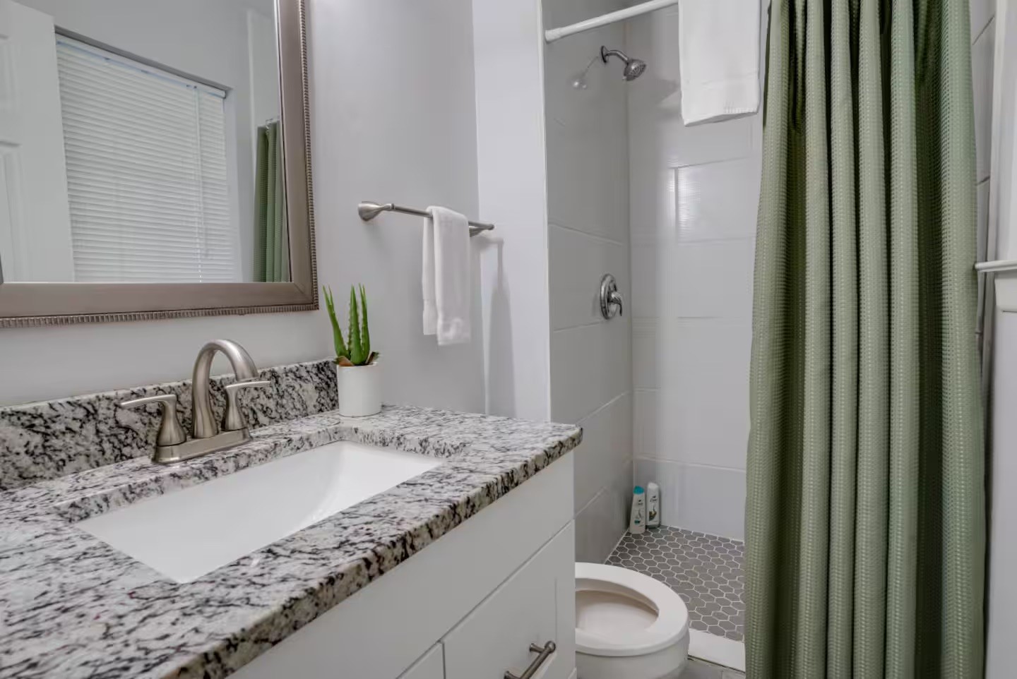 Bathroom with a granite vanity, framed mirror, and shower behind a green curtain.