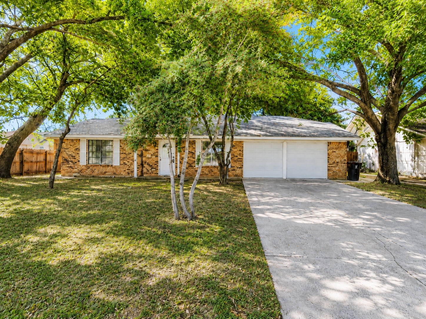 Single-story brick home with a two-car garage, shaded by mature trees.