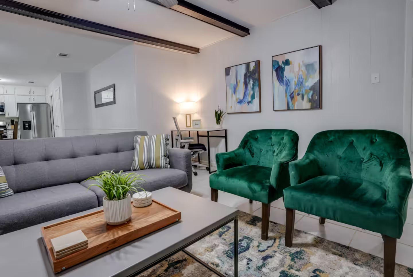 Living room with a gray sectional, emerald velvet armchairs, and exposed dark ceiling beams.