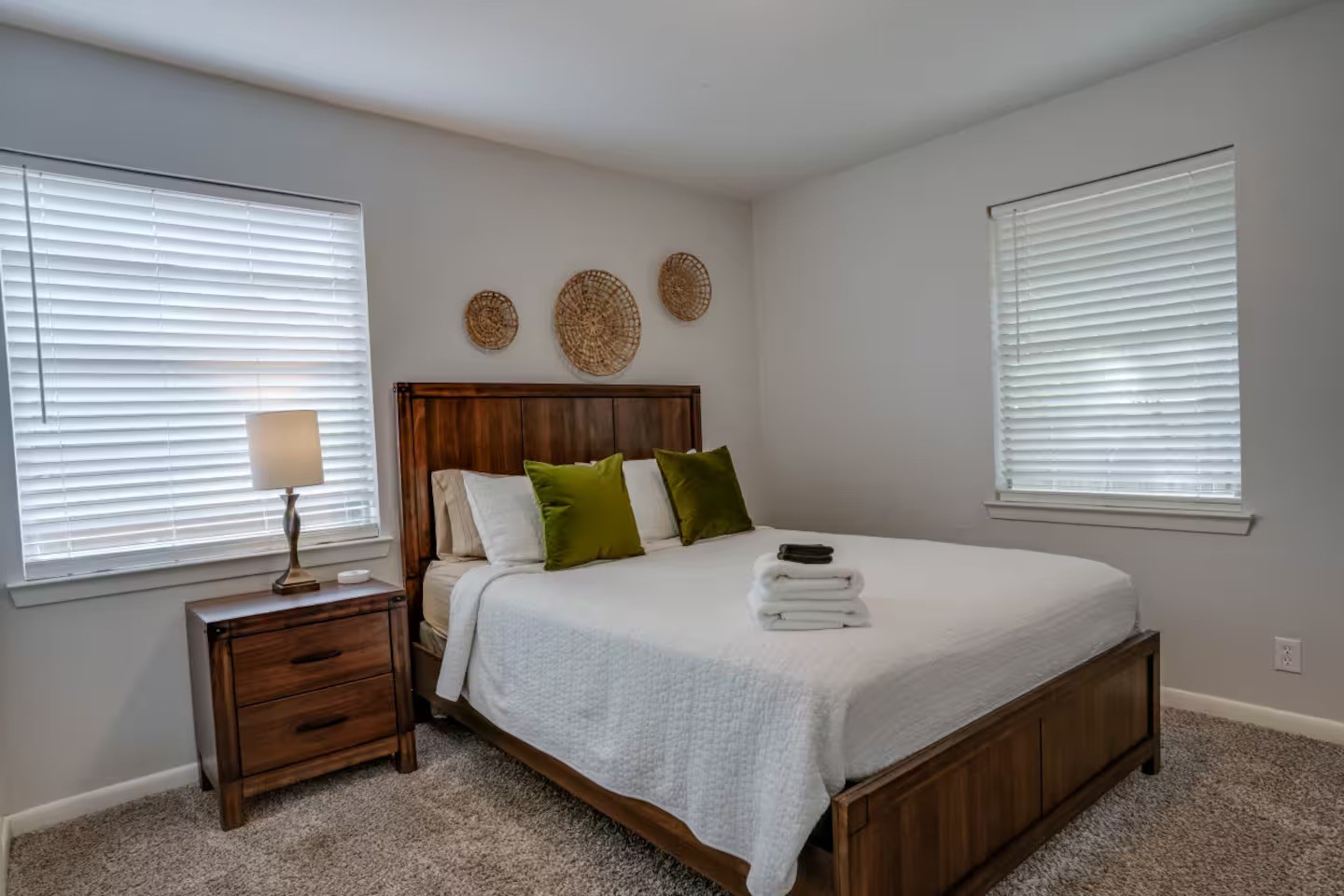 Bedroom with a wooden bed, white bedding, green pillows, and woven wall decor.
