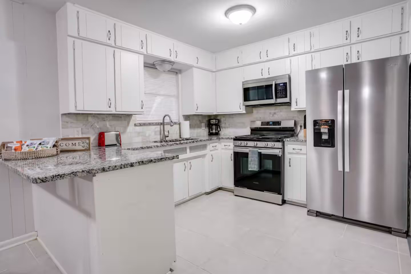 Bright kitchen with white cabinets, stone counters, and stainless steel appliances.