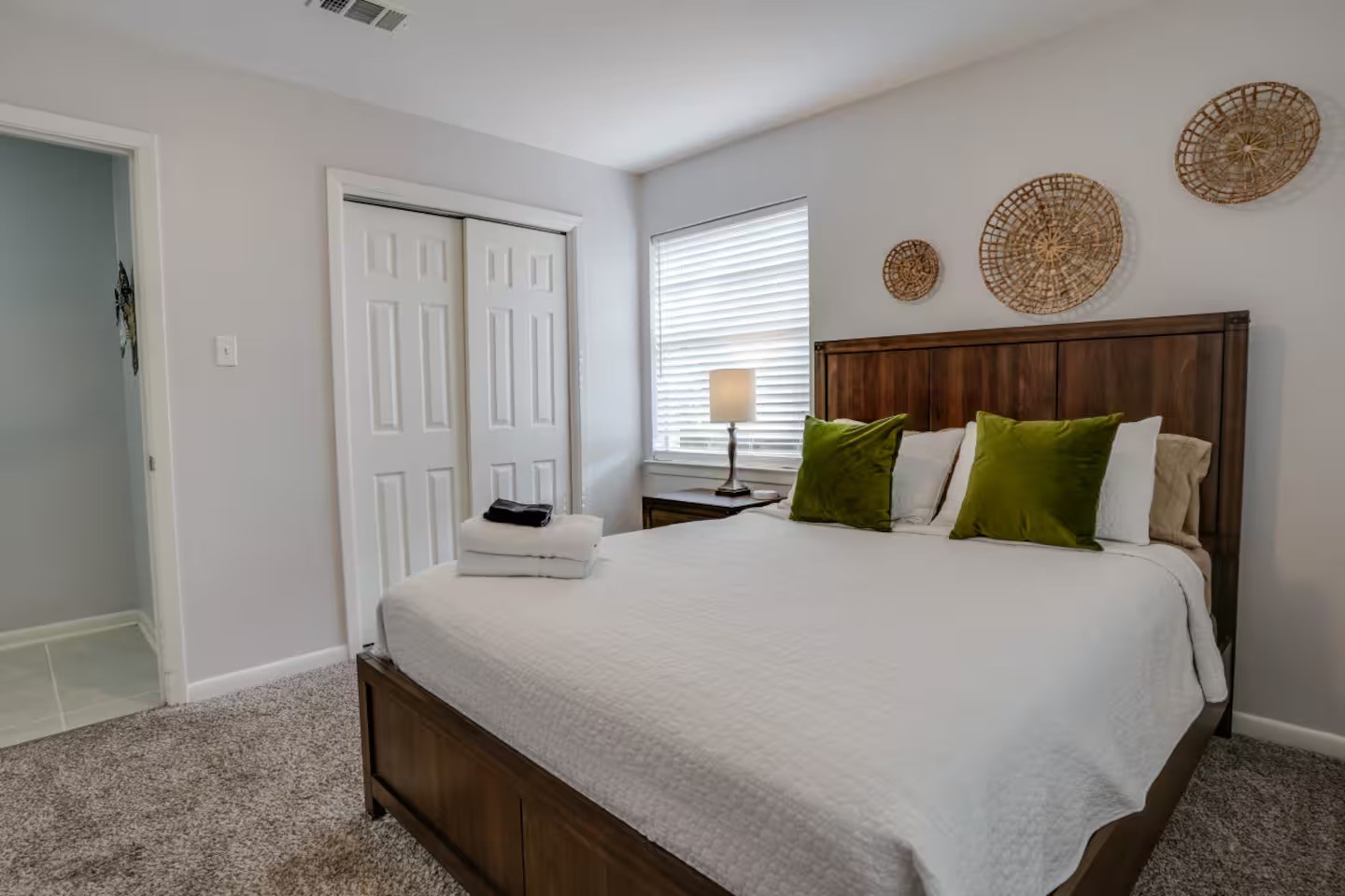 Bedroom with a dark wood bed, white bedding, green pillows, and woven wall decor.