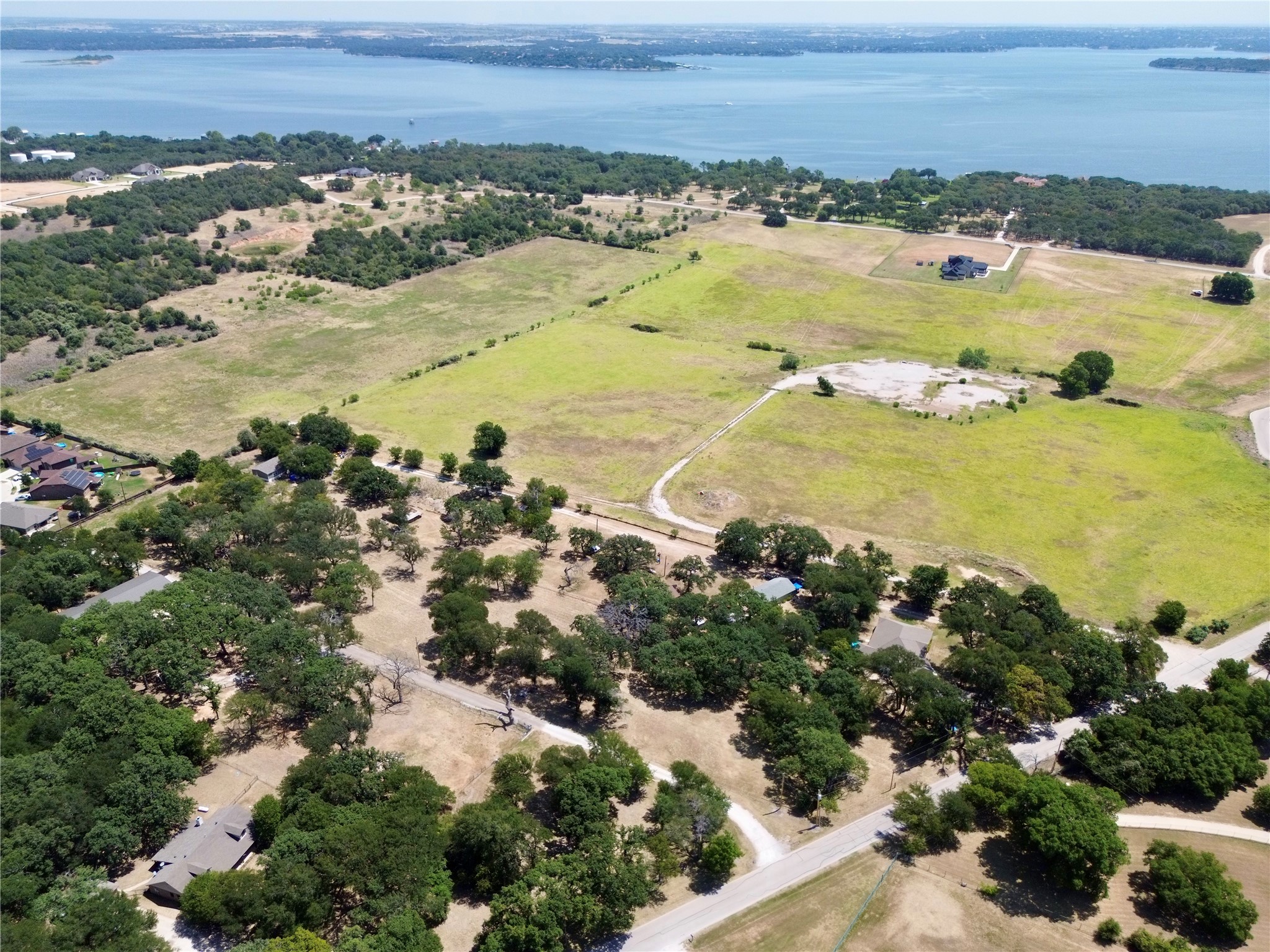 Aerial view of open grassy land with scattered trees and a lake beyond the shoreline.