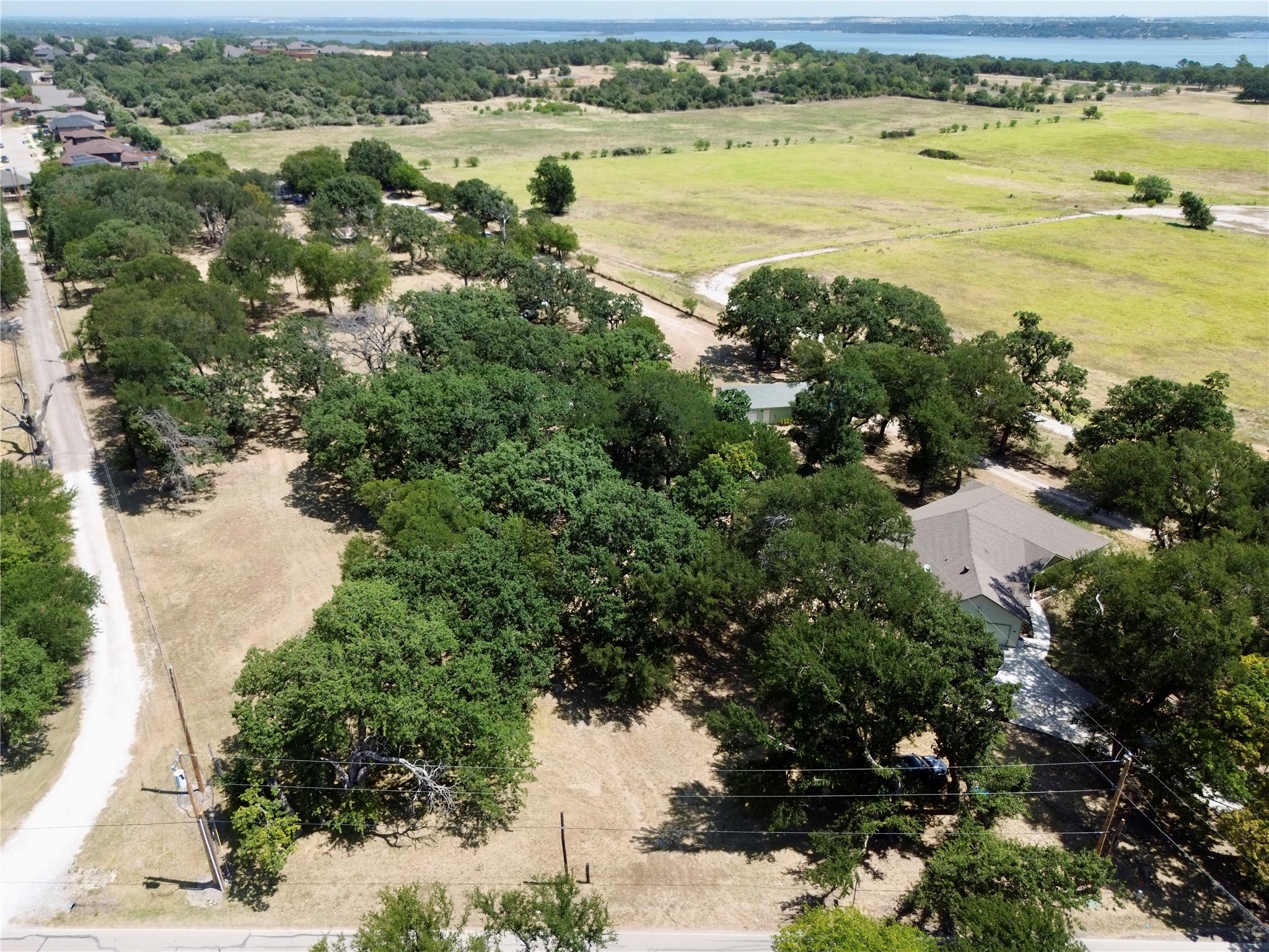 Aerial view of a tree-covered property with a house, open grassy areas, and water in the distance.