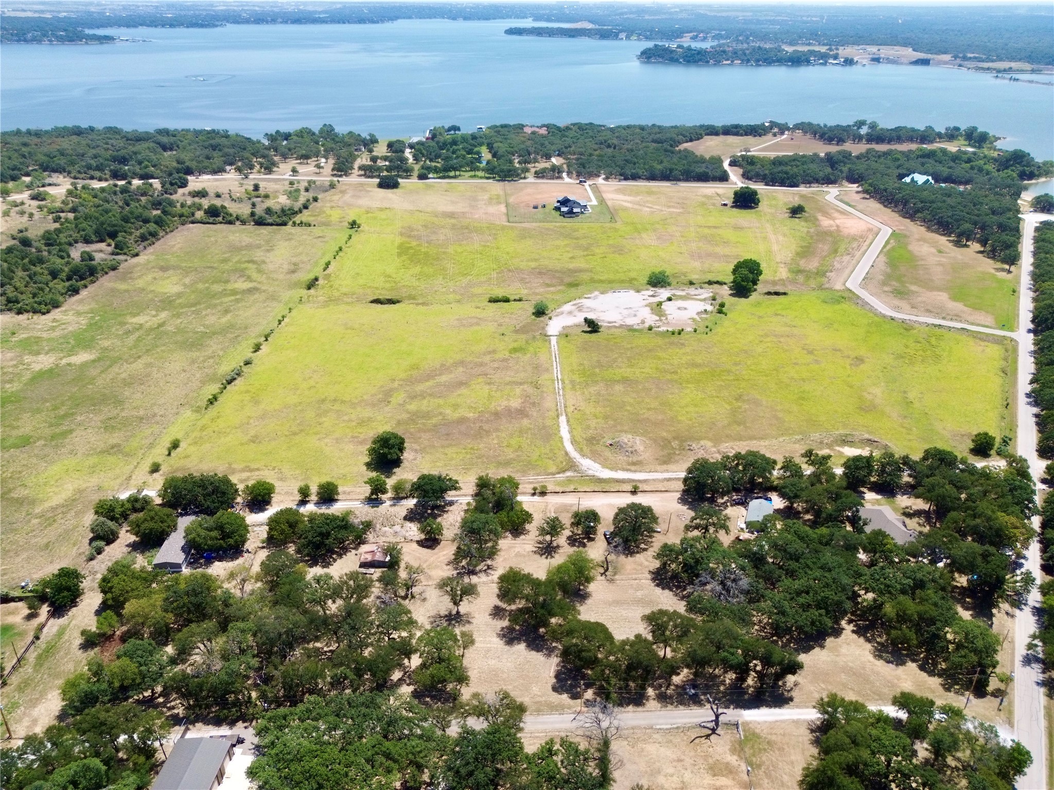 Aerial view of open grassy land with access roads and a lake beyond the wooded shoreline.