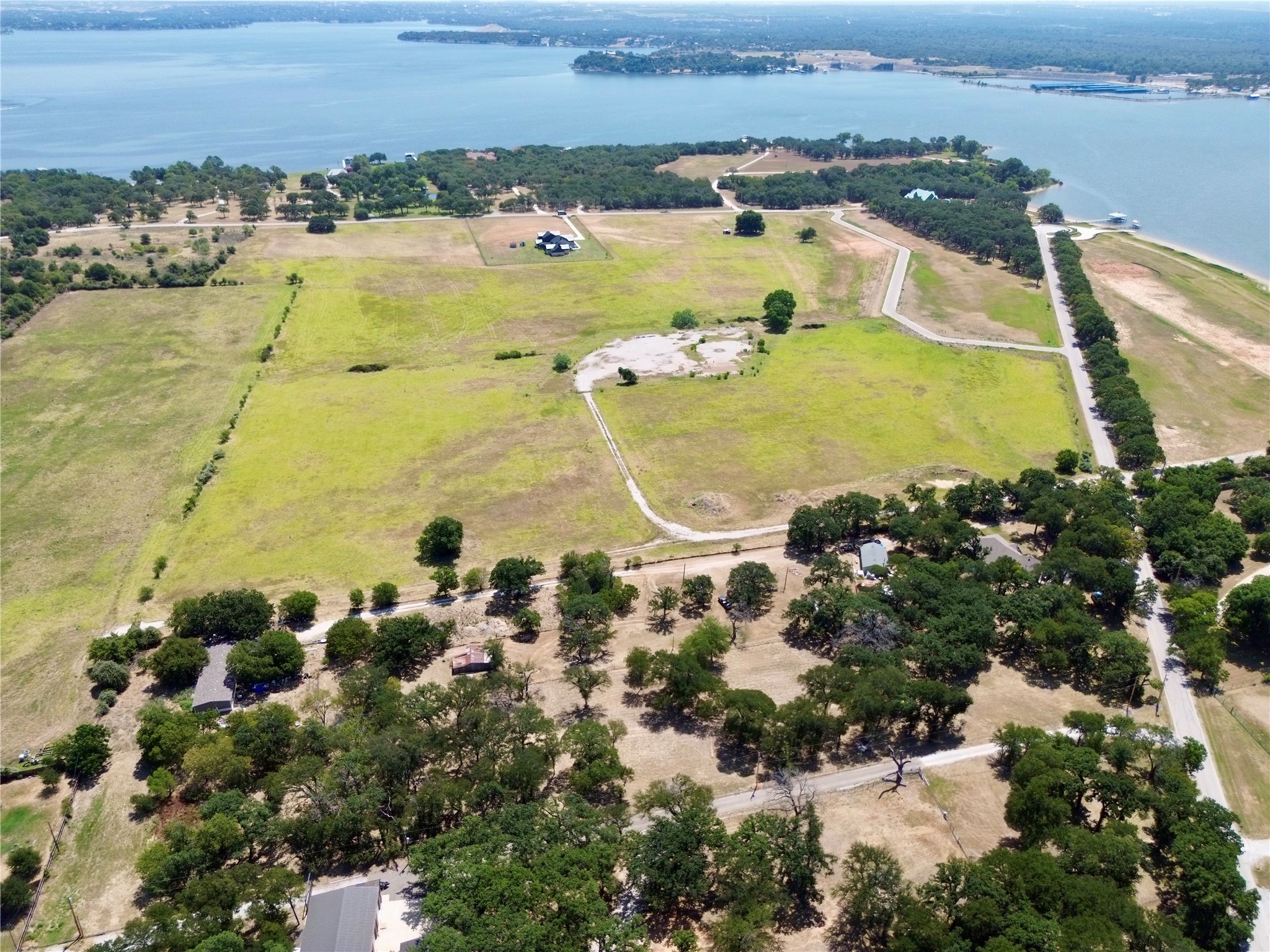 Aerial view of open grassy land with scattered trees beside a lake.