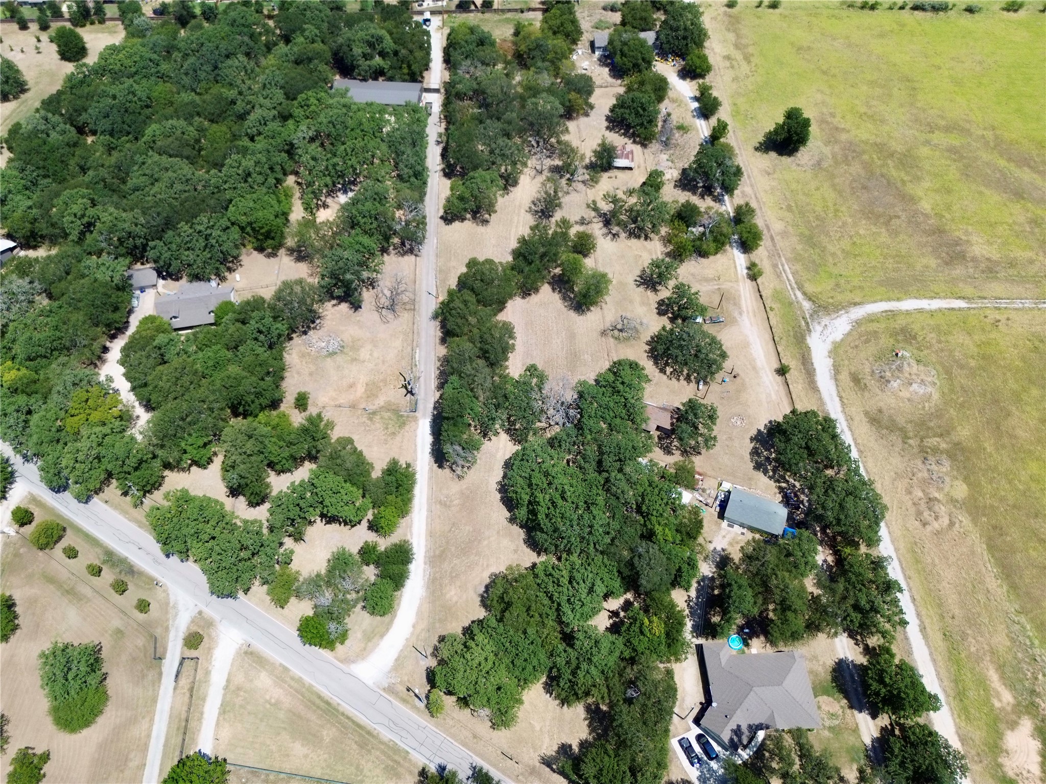 Aerial view of a wooded property with scattered buildings, open land, and gravel drives.